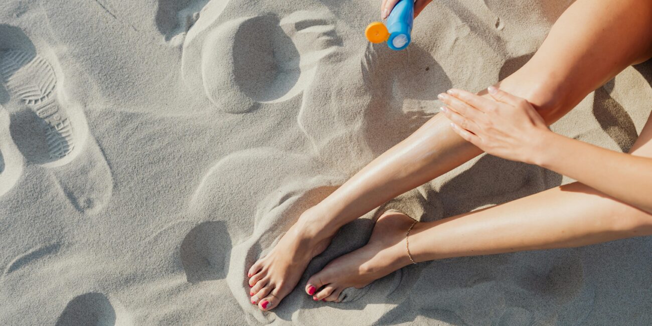 woman on the beach applying sunscreen to her legs