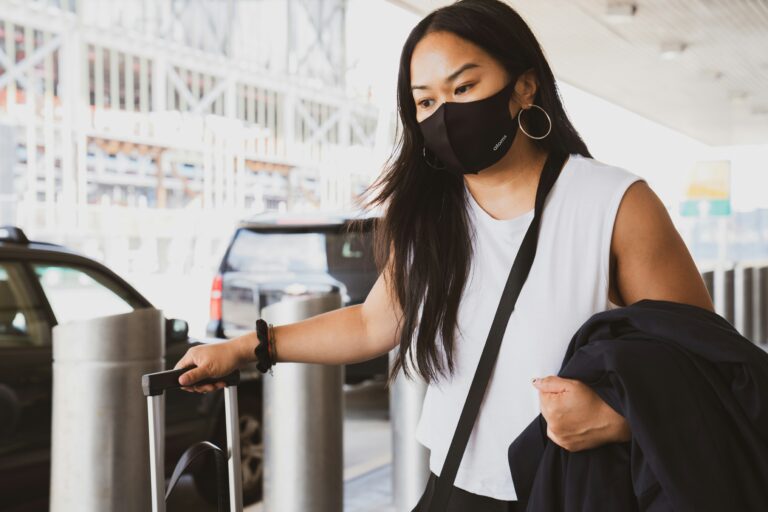 Woman outside airport wearing a face mask and pulling a suitcase