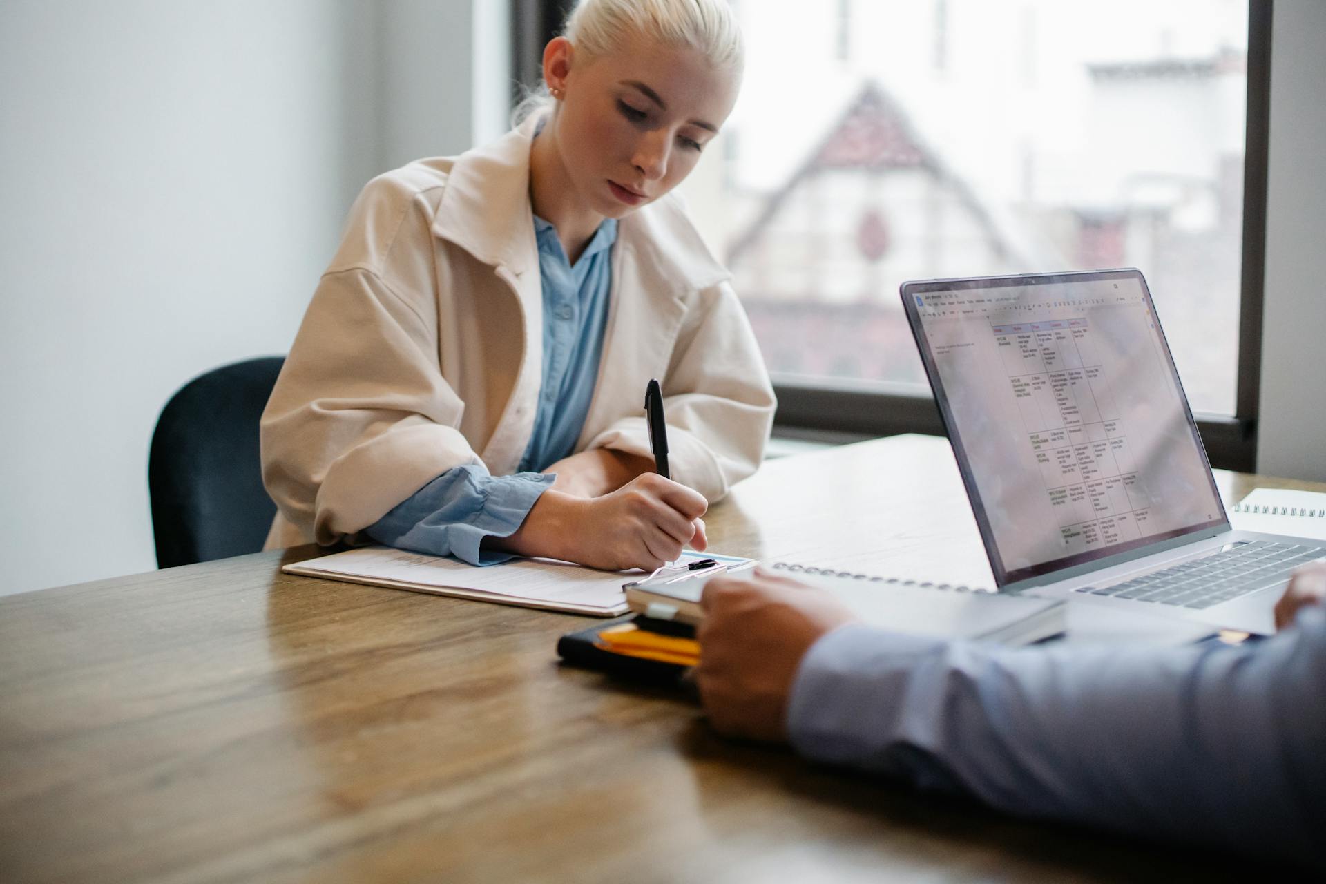 Woman sits across desk signing documents