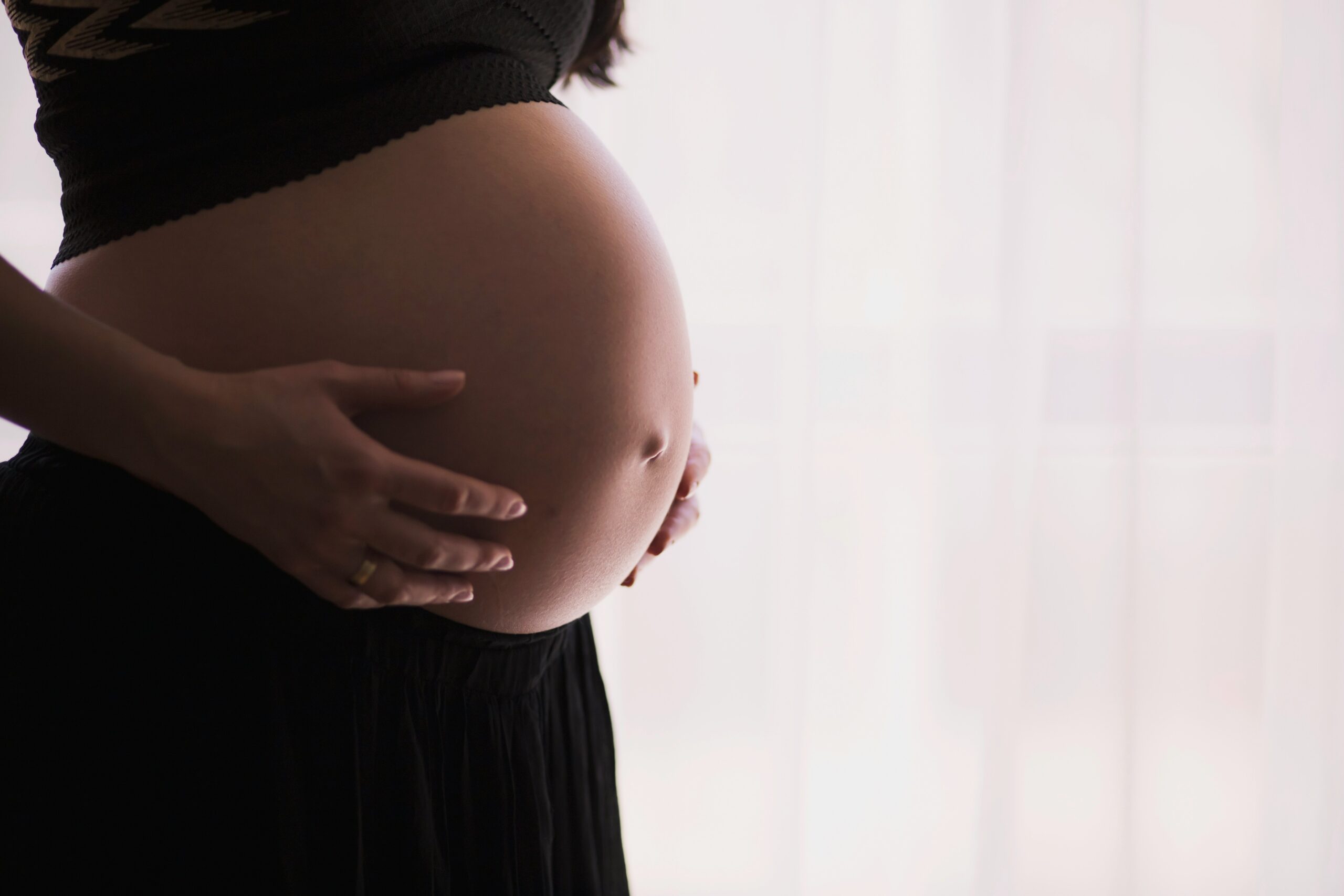 dark close up of a woman from the side holding her bare pregnant stomach