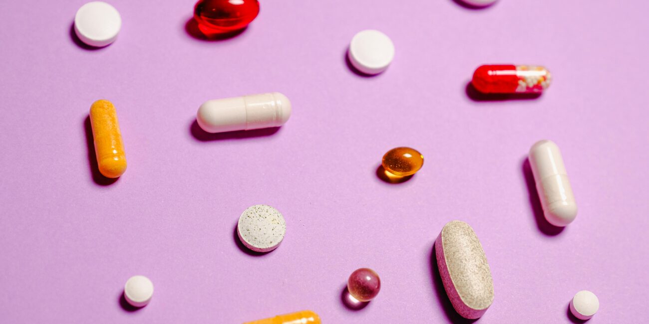 A pink background with different supplements and vitamins scattered across it