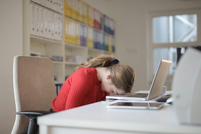A tired woman sits at a desk with her head on the table