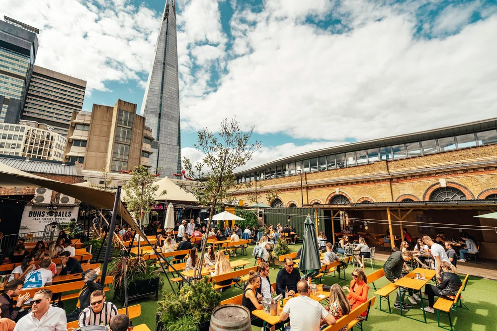 A collection of tables next to a railway arch in the shadow of the Shard.