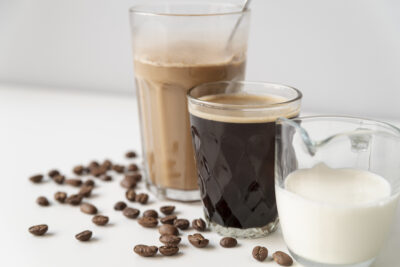 an iced coffee, a black coffee and milk all sit by by side in glasses on a white table