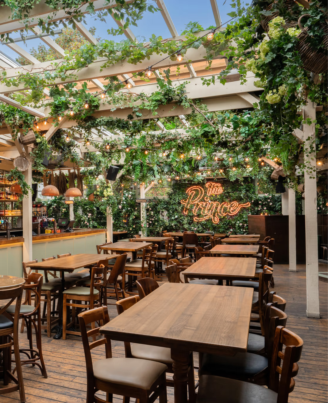 Wooden tables beneath a wooden pergola covered in plants.
