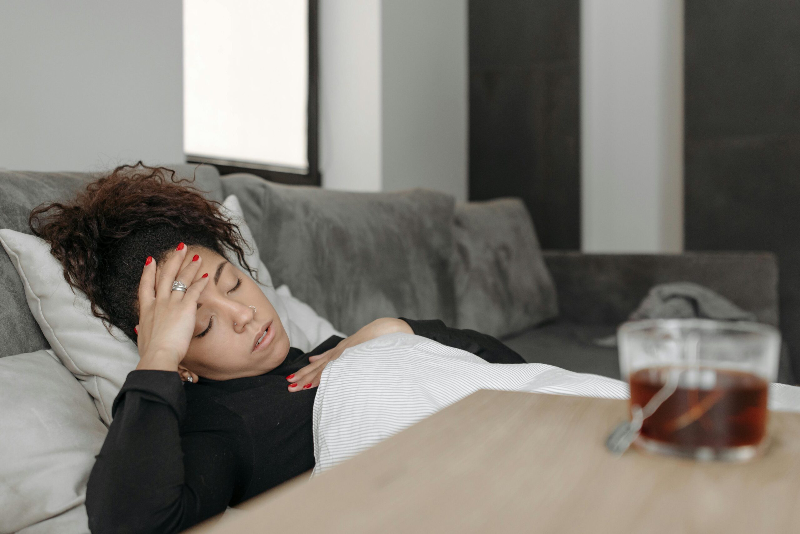 a woman with a migraine lies on the sofa holding her head