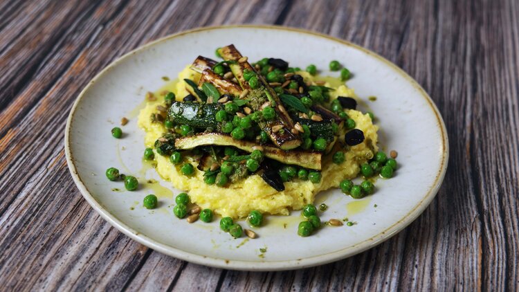 A plate of polenta topped with peas and courgette.