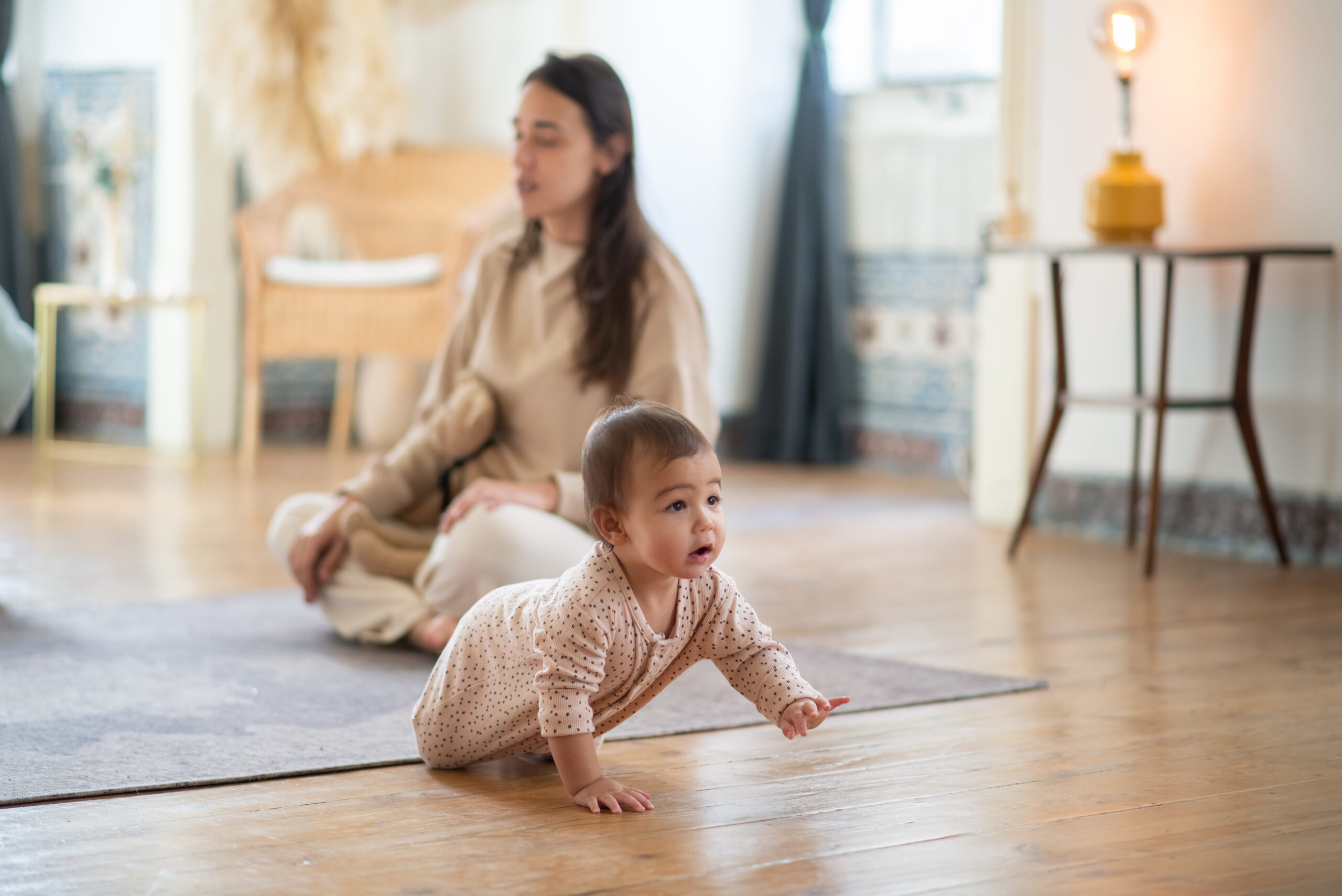 baby crawls while a woman does yoga in the background