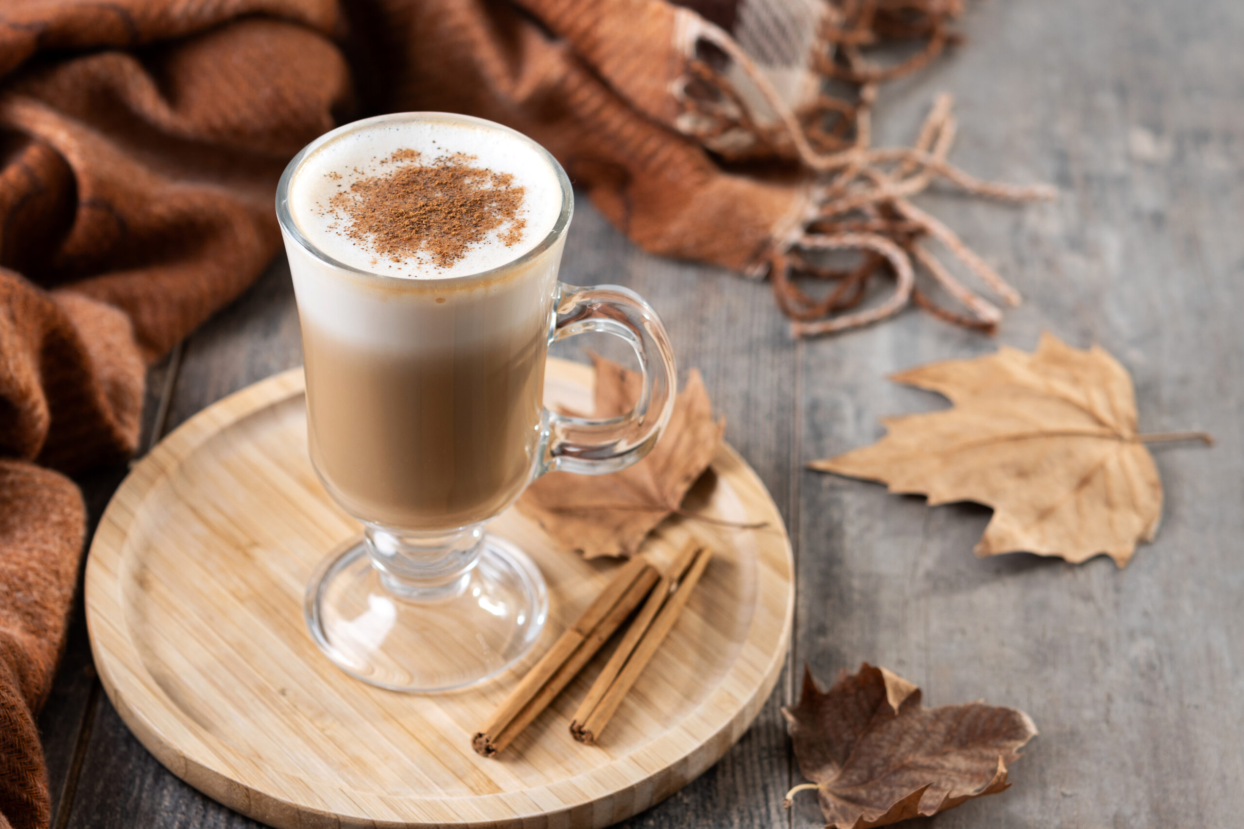 A glass filled with pumpkin spice latter sat on a wooden board.