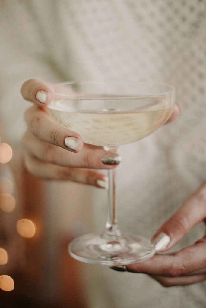 A hand with gold-painted nails holds a champagne glass