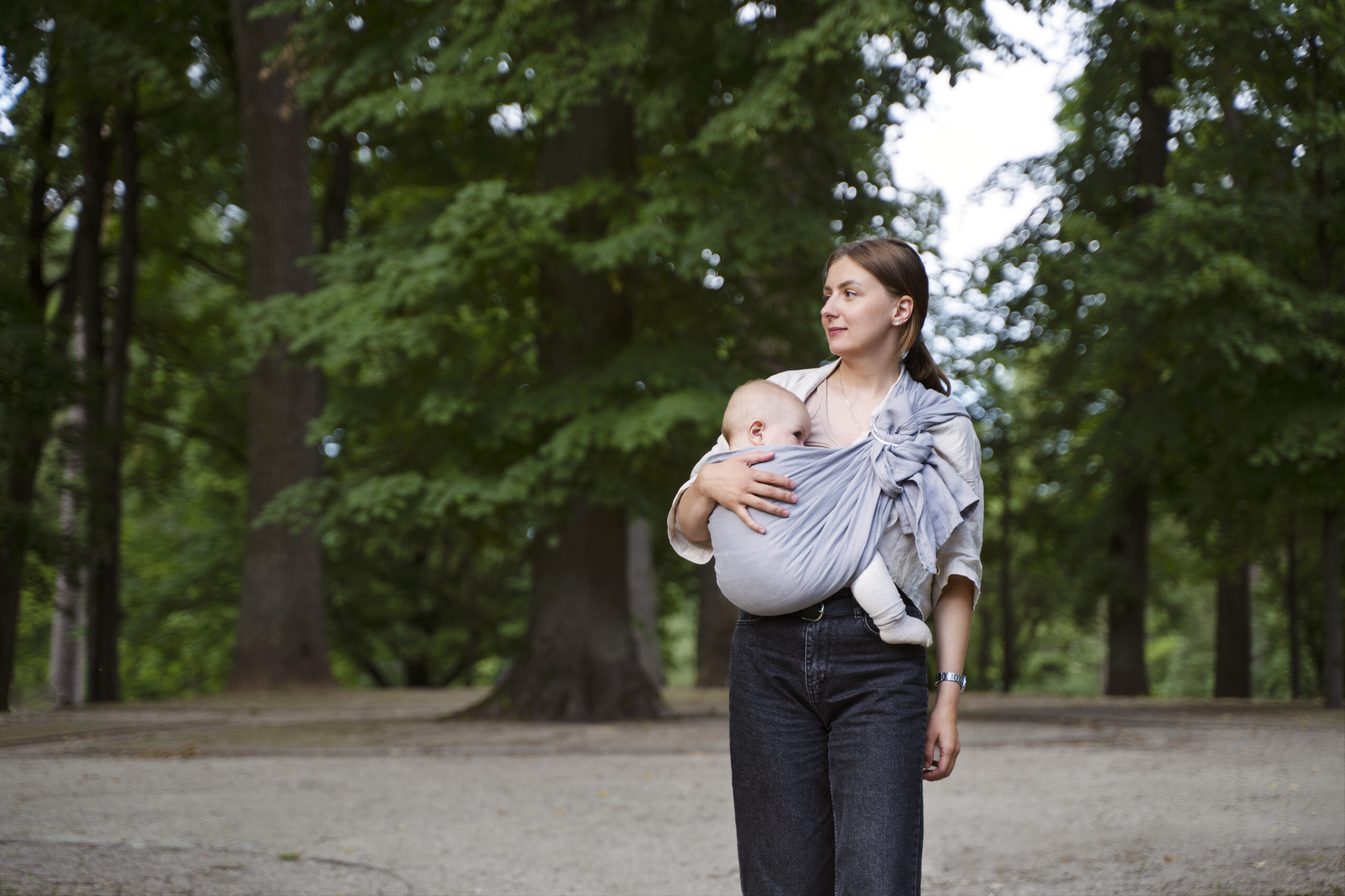 woman walks outside carrying her baby in a sling