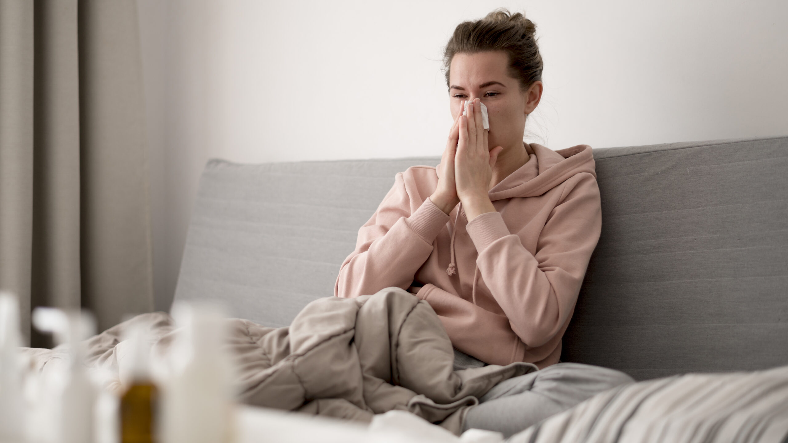 woman in bed blowing her nose due to allergies