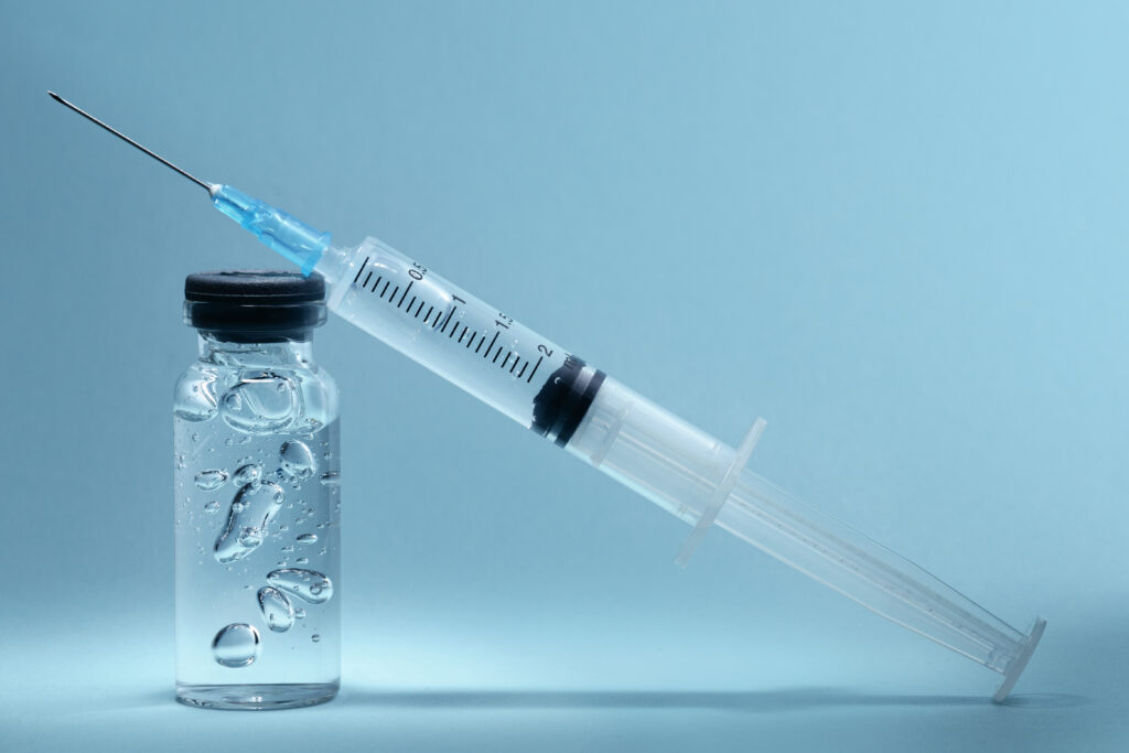 A syringe perched on top of a vial filled with salmon sperm serum.