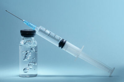 A syringe perched on top of a vial filled with salmon sperm serum.