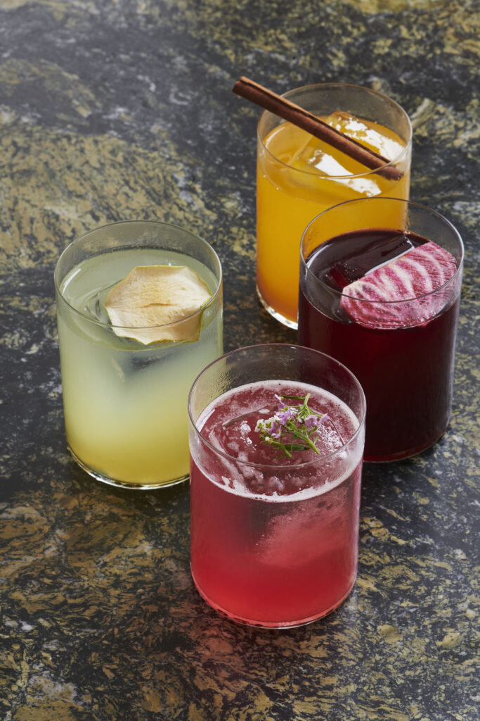 Four colourful cocktails on a table with spices in