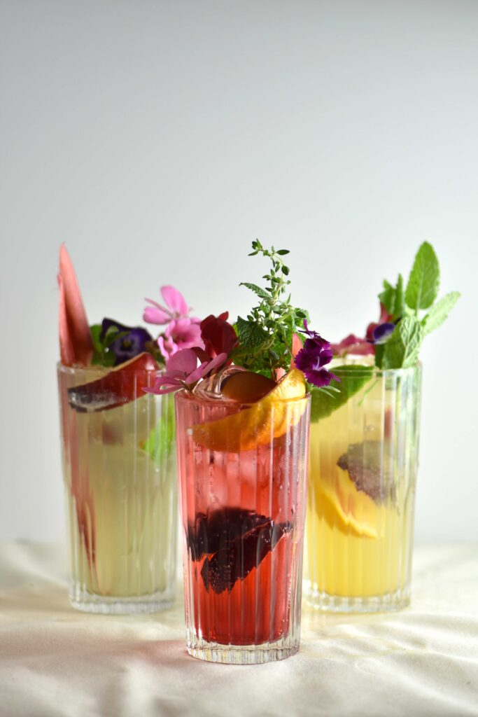 three colourful mocktails with fruit and leaves and plants