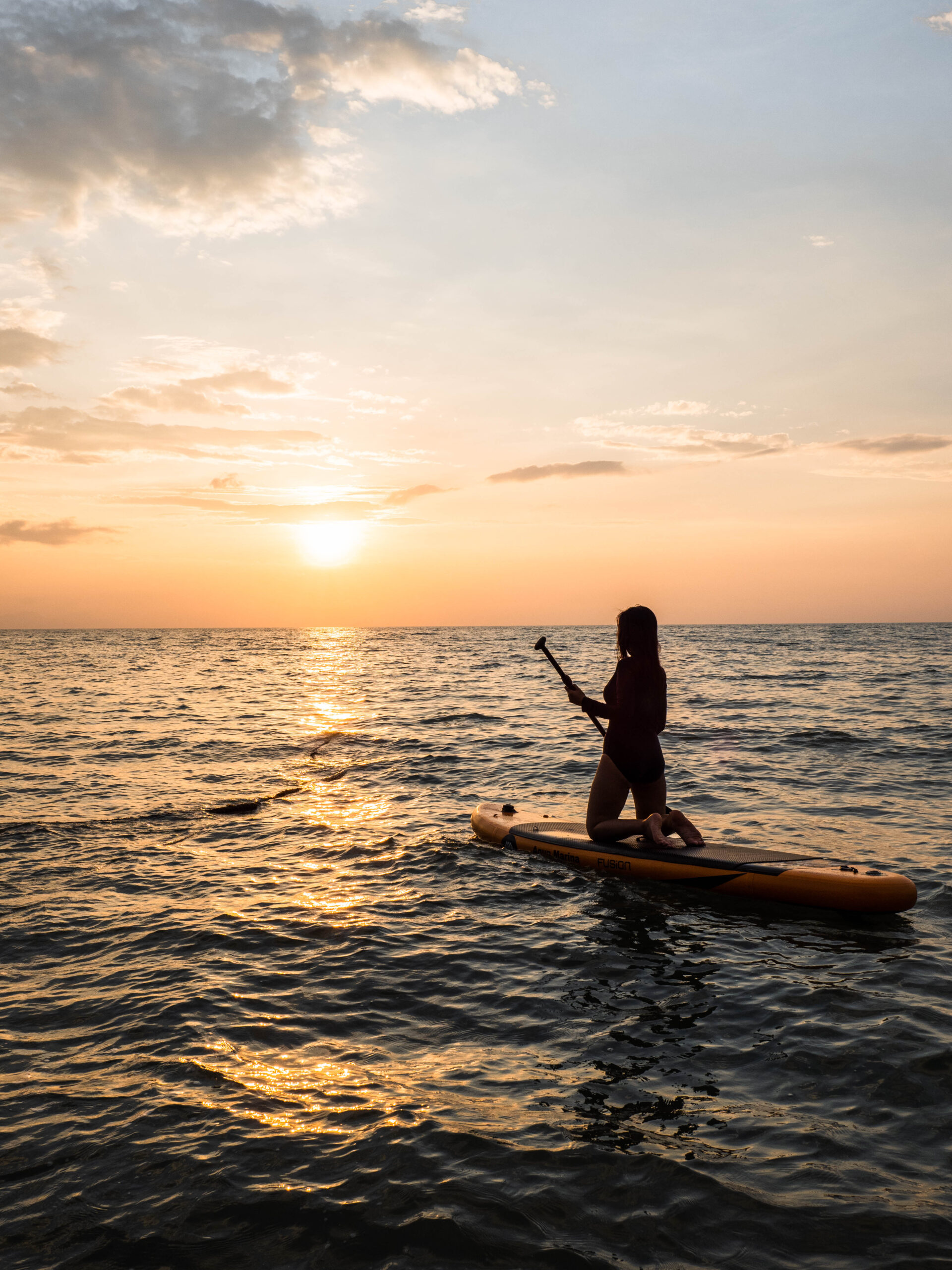 Sunset view of beach with woman kneeling on stand up paddleboard