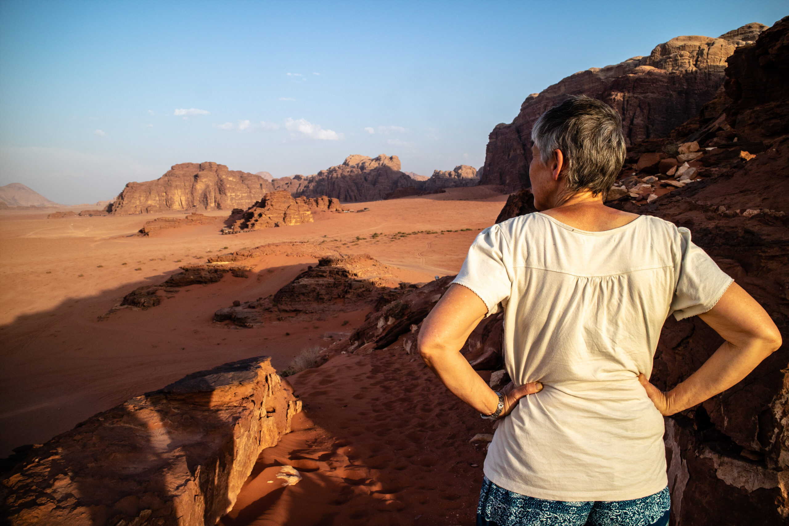 Woman standing with her back to the camera overlooking desert and mountains as orangey sun sets 