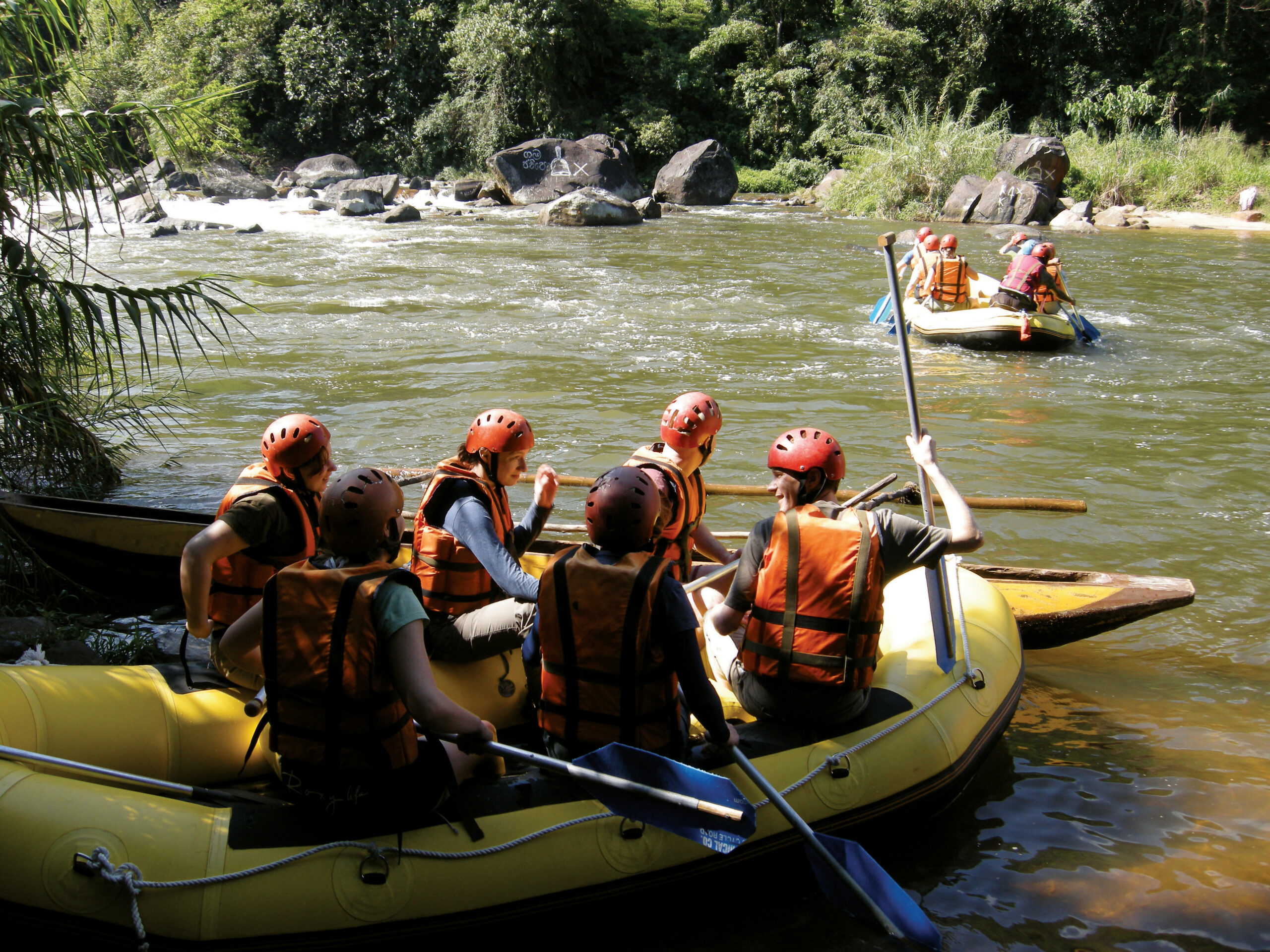 Three rafts with people aboard holding oars on a river in Sri lanka