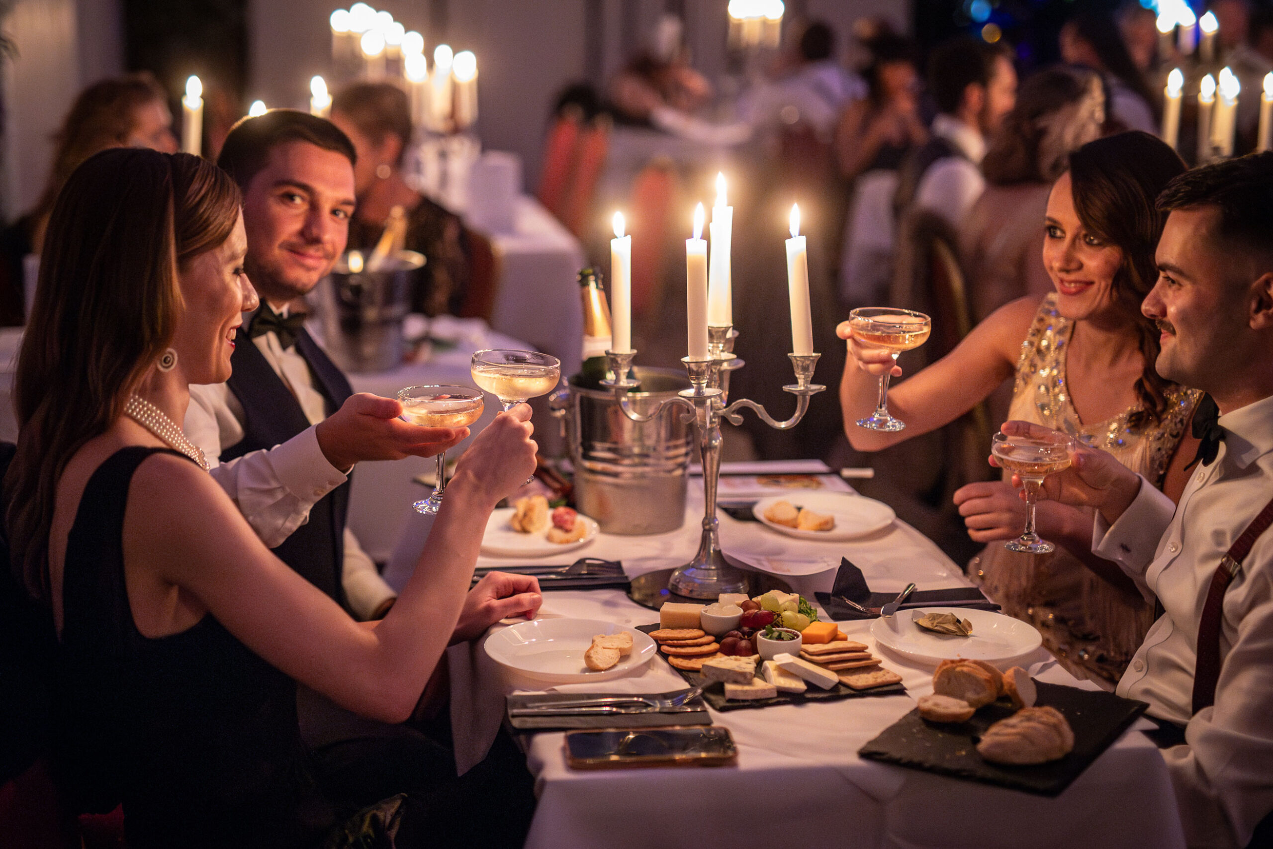 Diners in formal 1920s clothes sitting at a meal by candelight