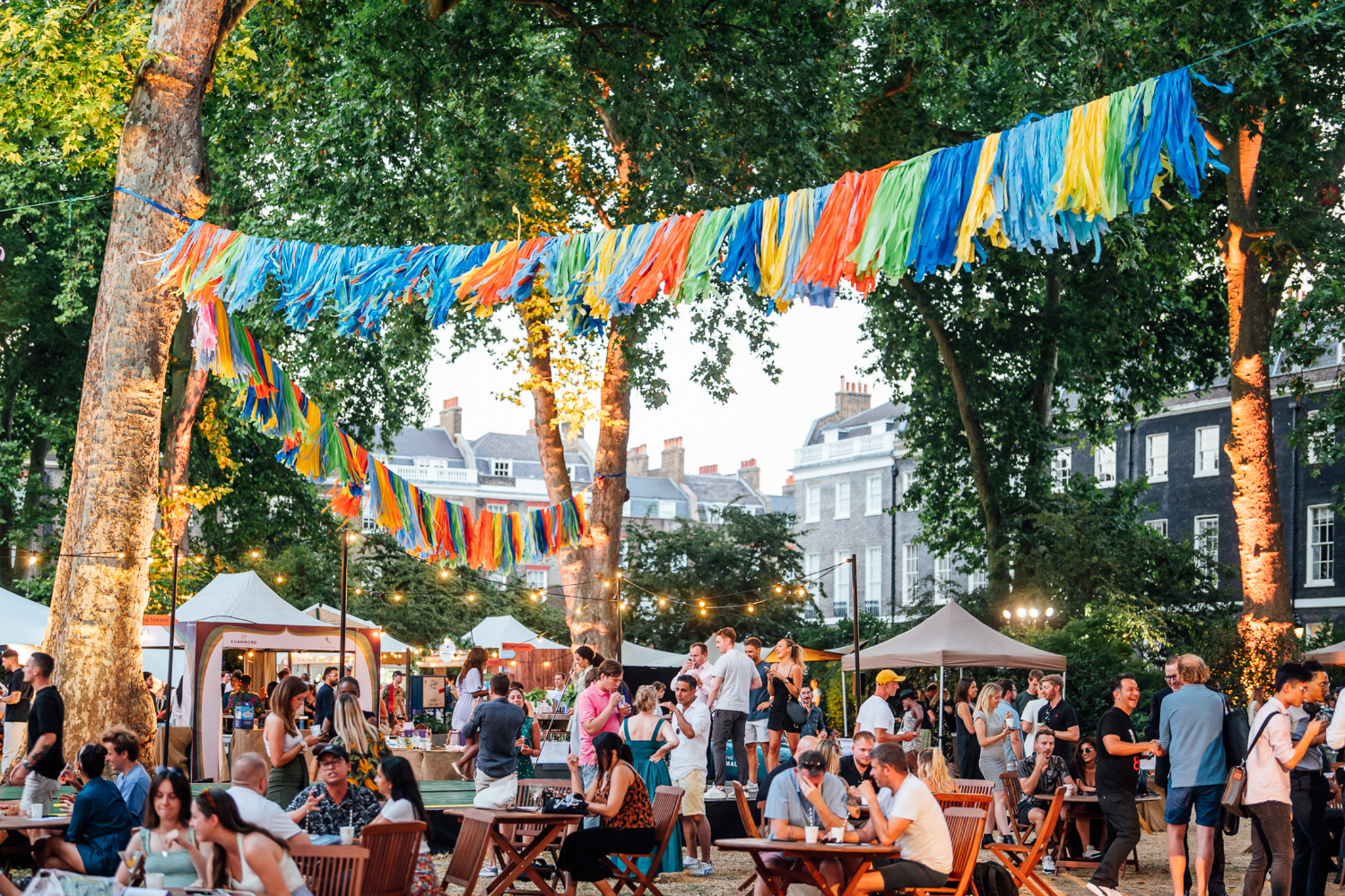 Garden square filled with bunting, tables and chairs and marquees where attendees sip cocktails