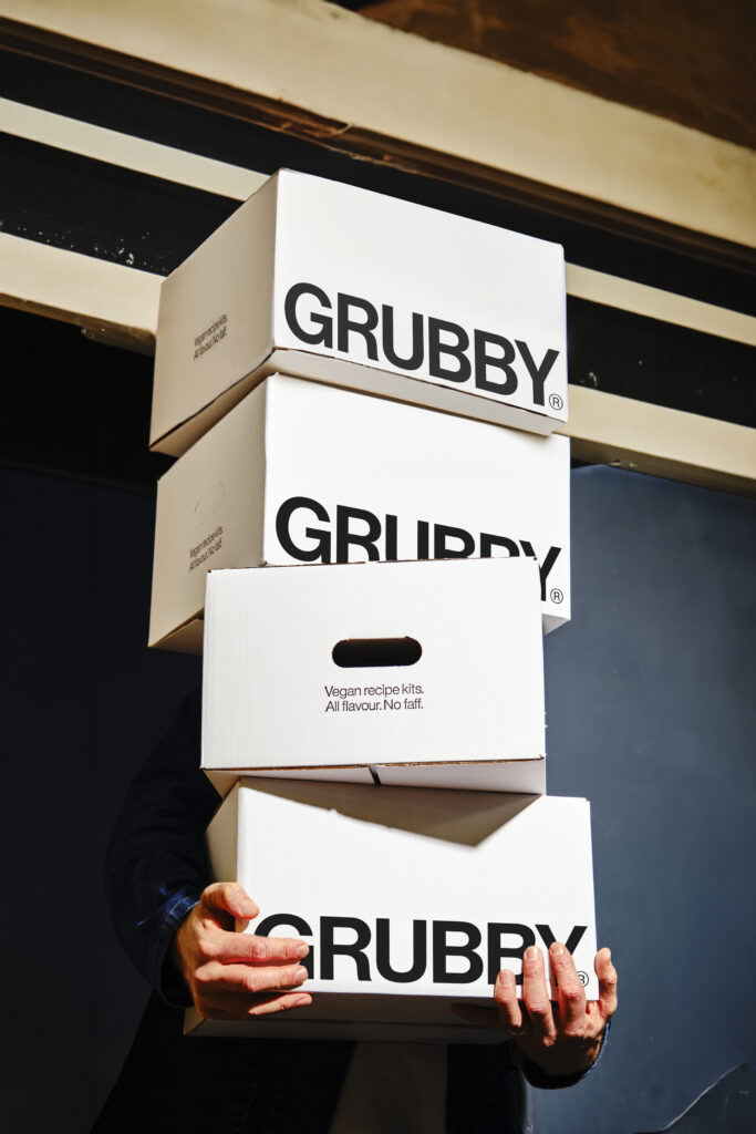 navy background and hands holding three white stacked white boxes with grubby branding