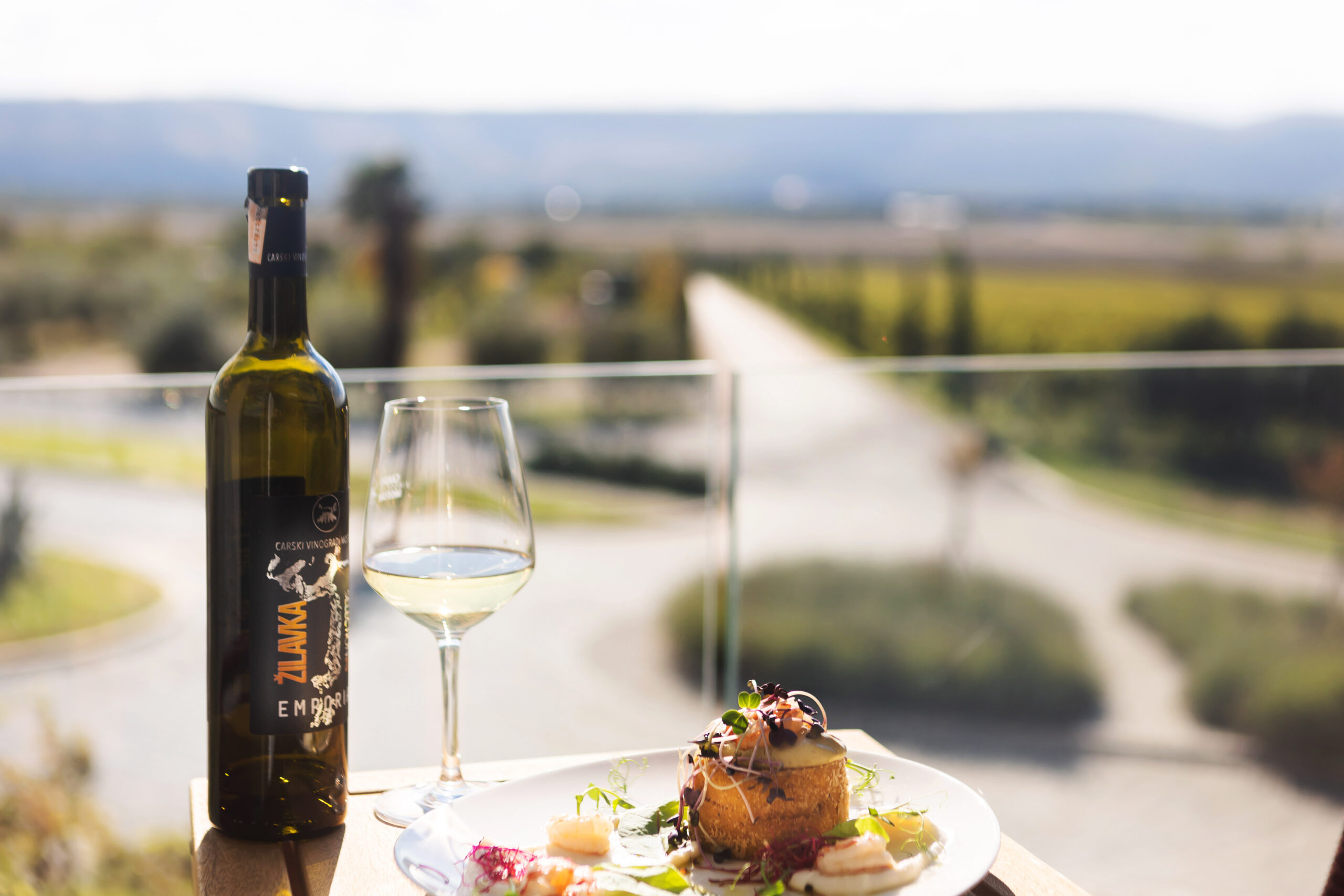 balcony view with a table with plate of food on top and a wine glass with wine in and bottle