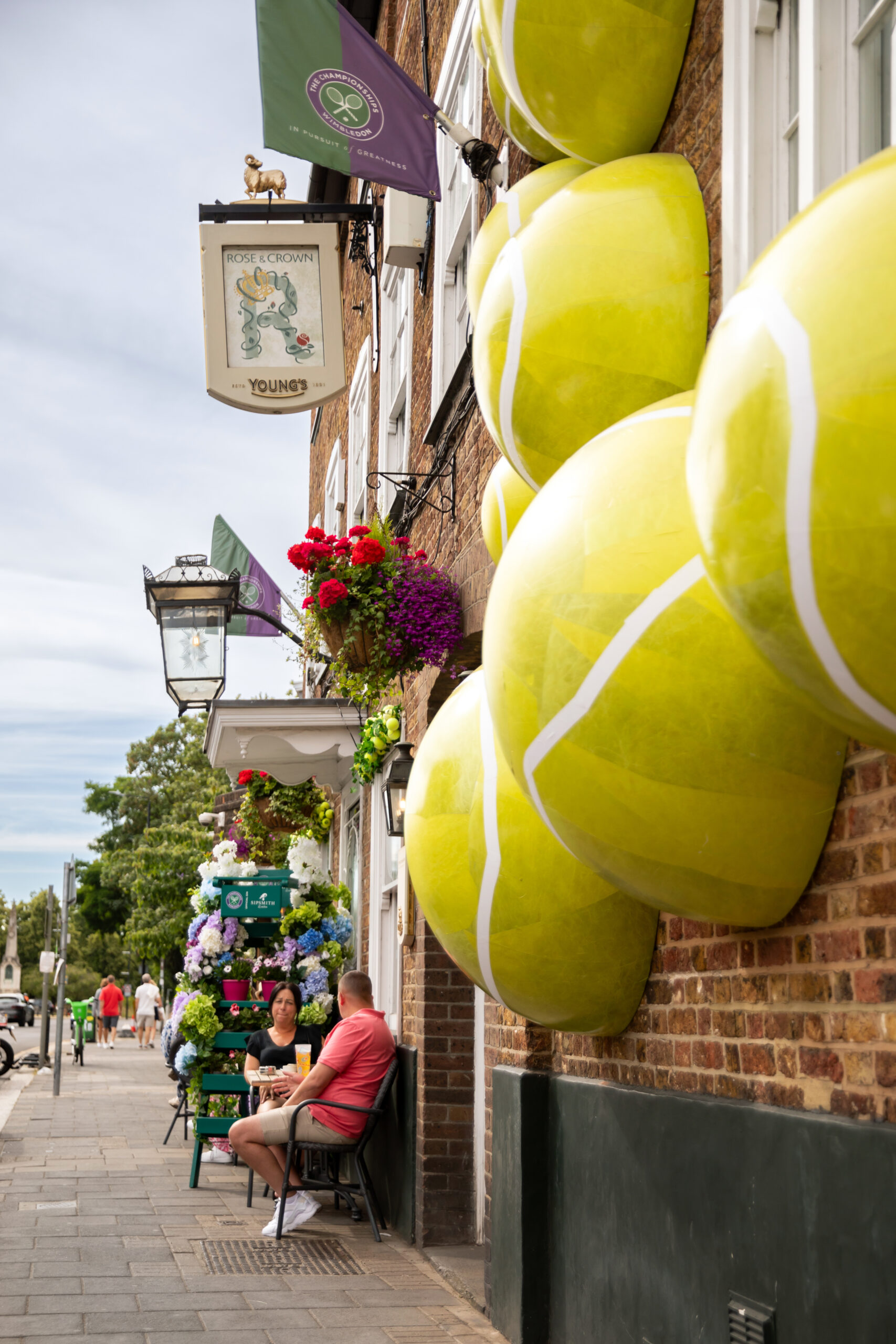 exterior of a pub with bricks, people sitting outside at tables and large tennis ball half moons protruding from the edge of the wall
