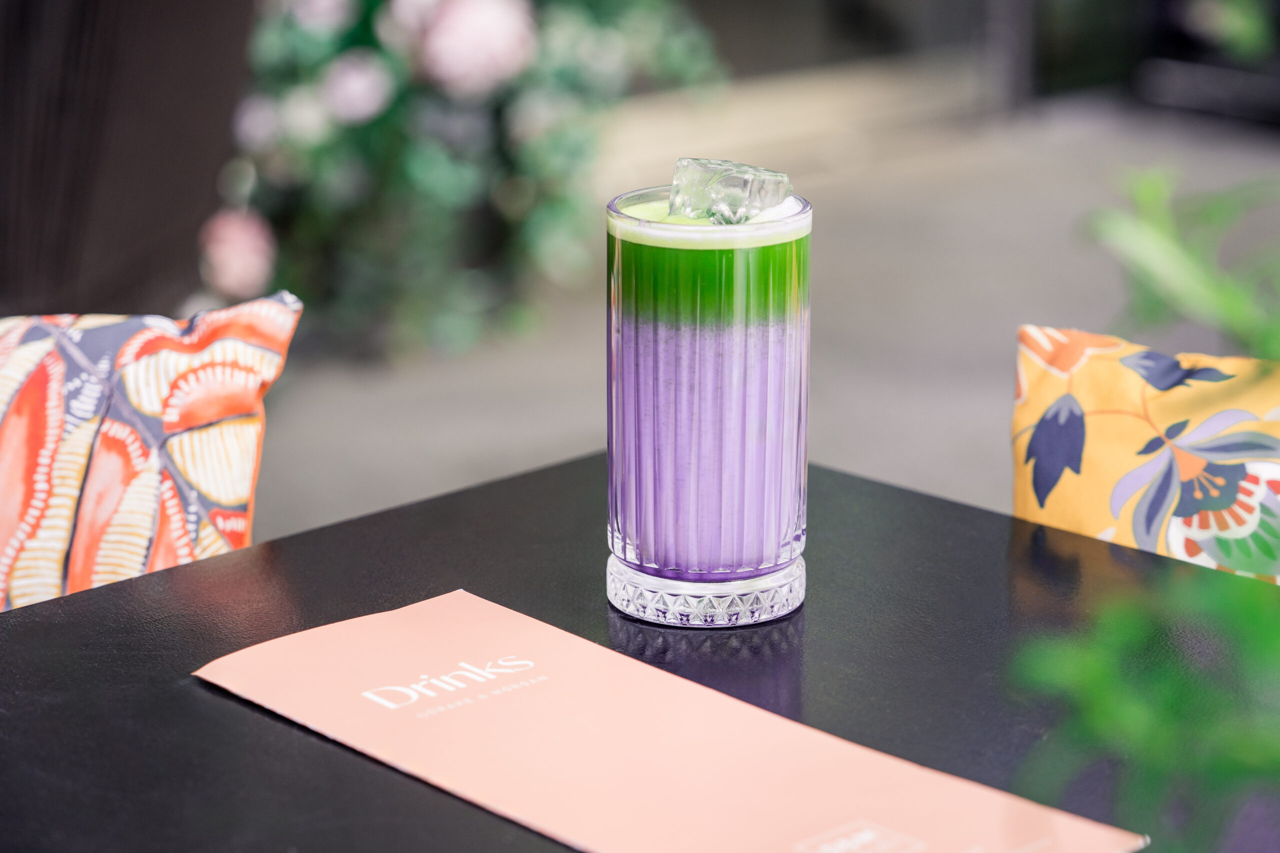 Black table with a glass with matcha in that is coloured purple and green with ice