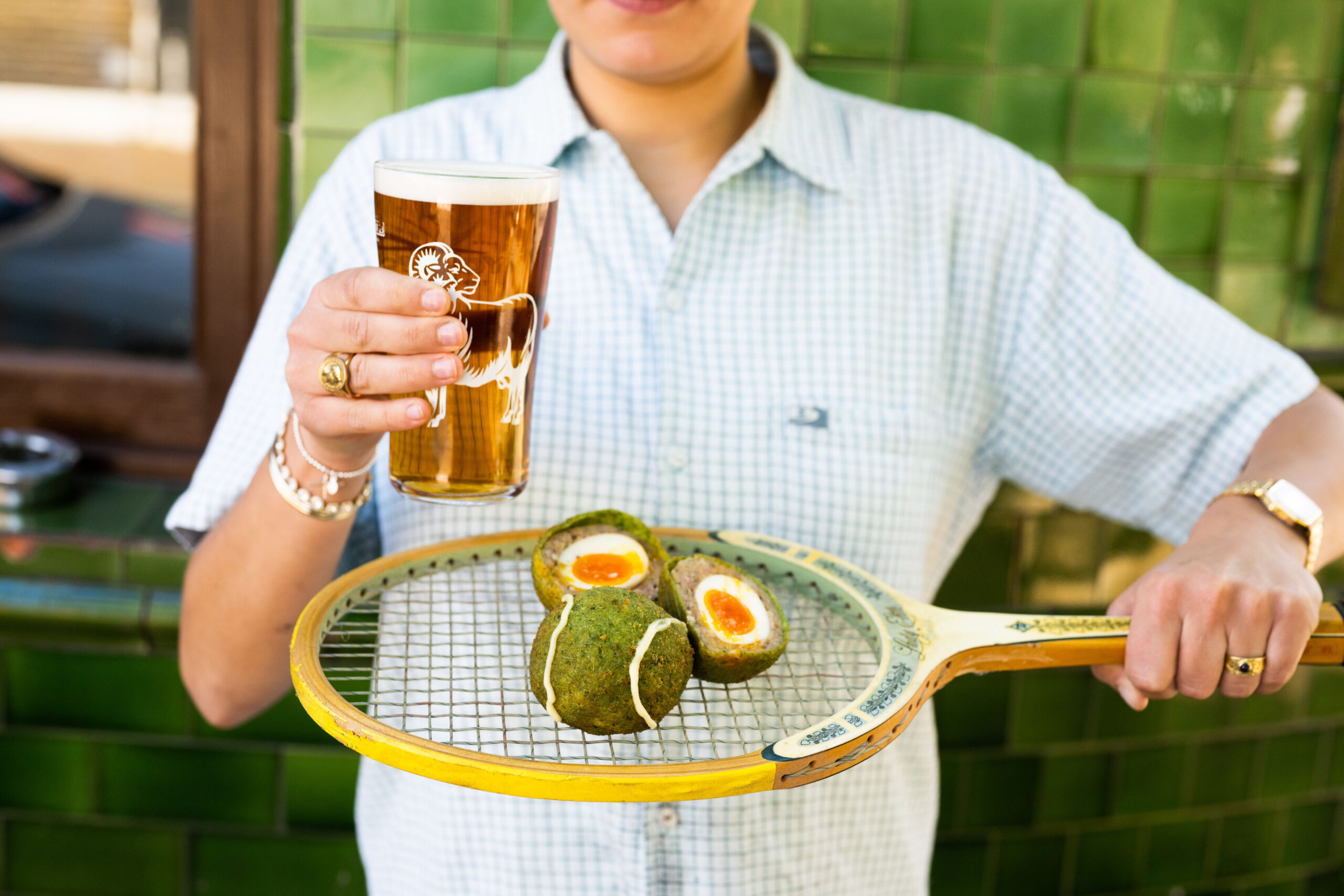 man holding tennis racket with tennis ball scotch egg and beer