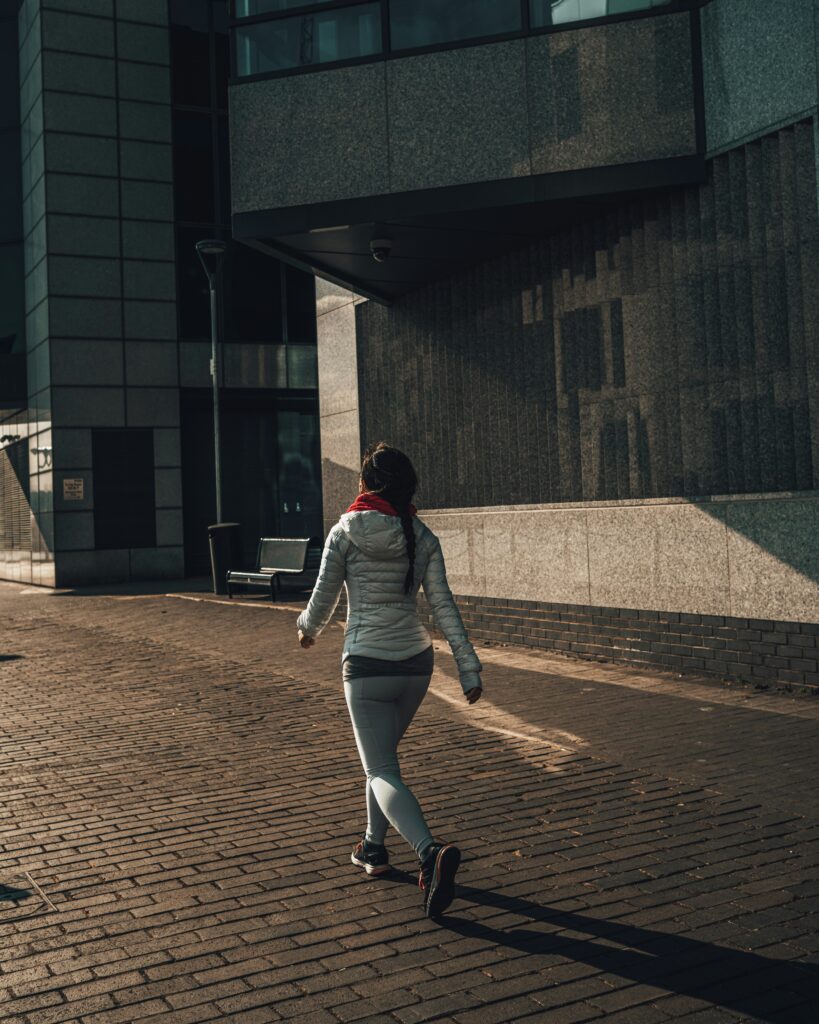 woman in workout clothes walking through a city with concrete buildings