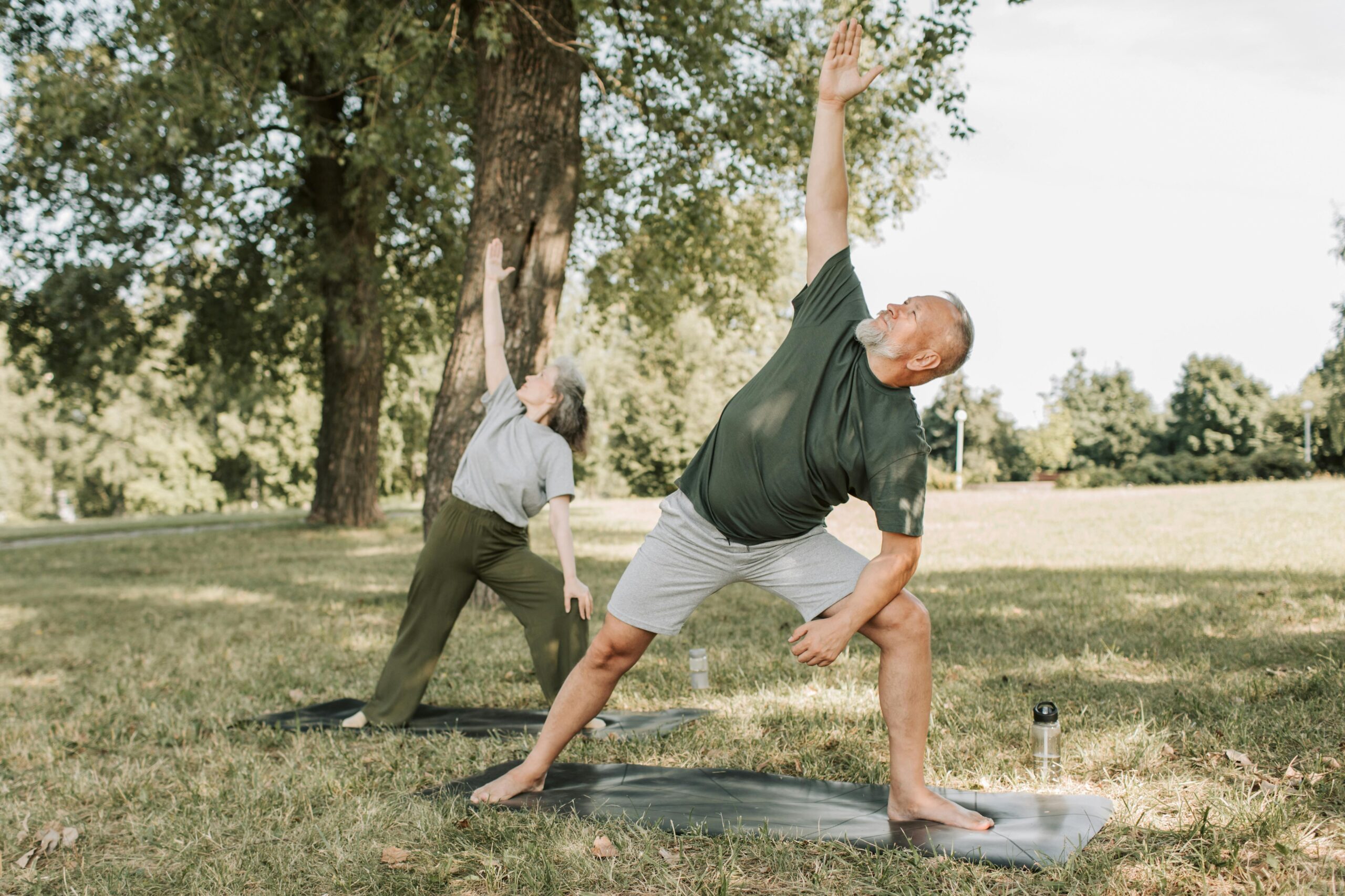 a man and a woman in green neutral clothes doing yoga in a park on yoga mats
