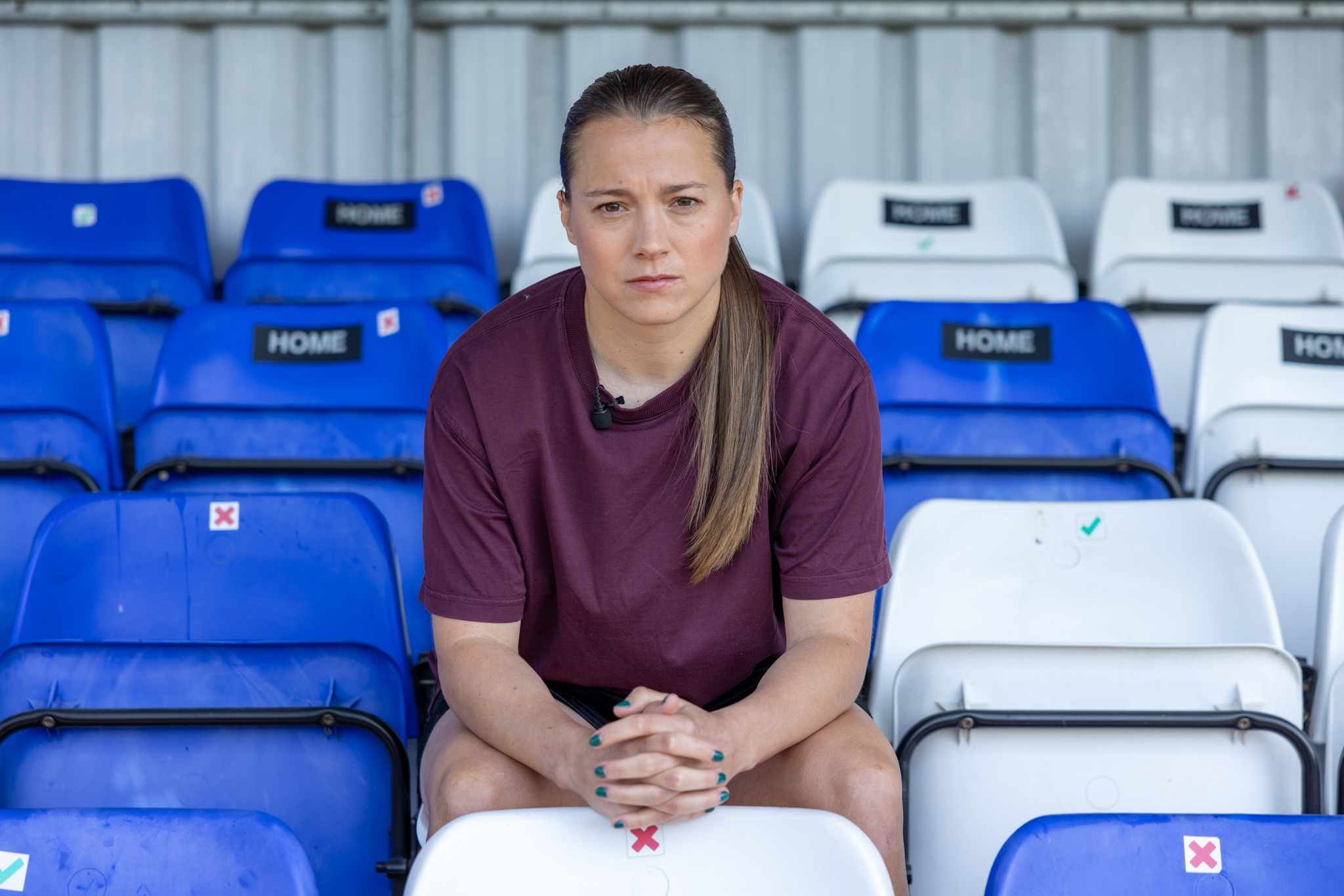 football stadium stands with blue and white stadium chairs where female footballer Fran Kirby sits in the middle with hands clasped together