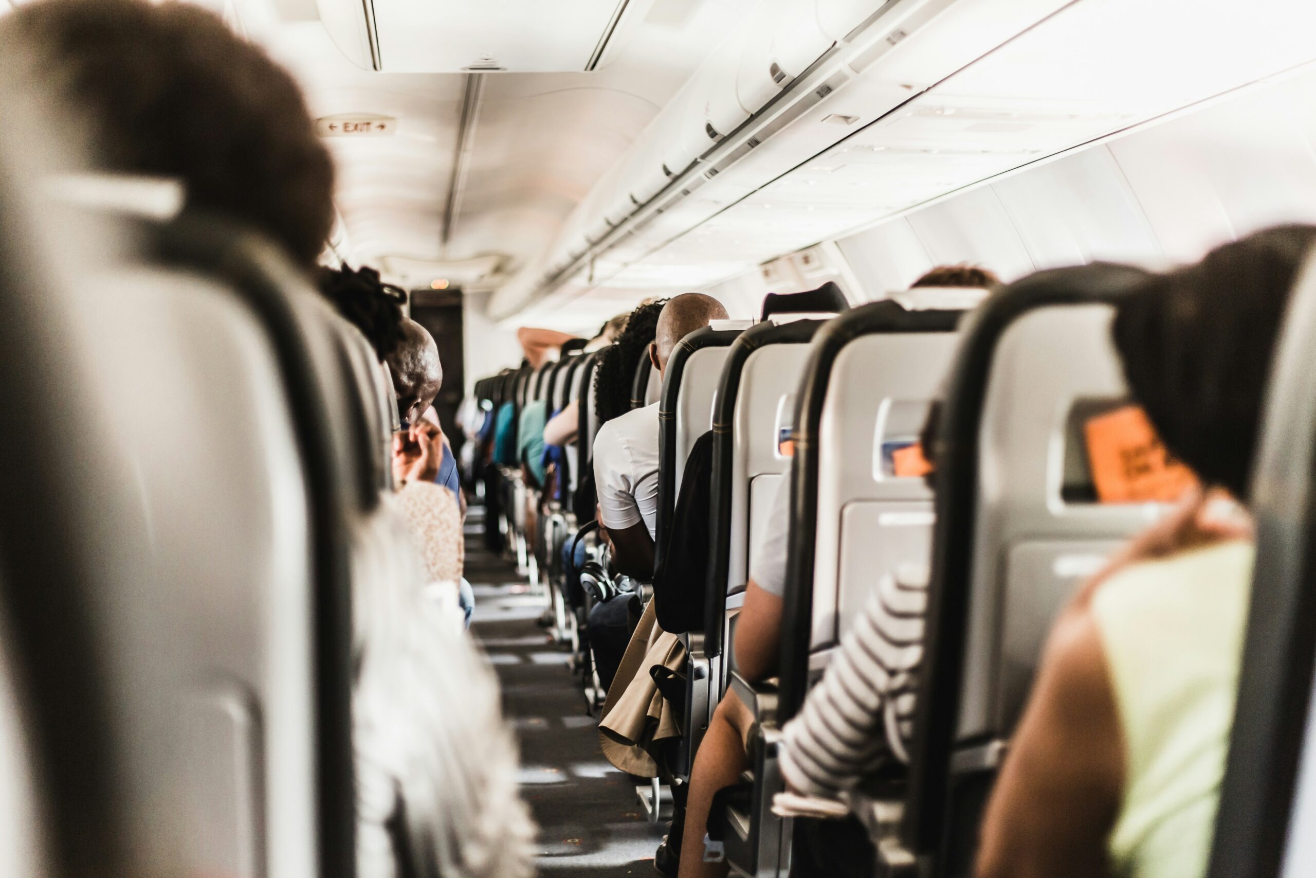 back view of a plane aisle with people sitting in and arms on the chairs in the aisles