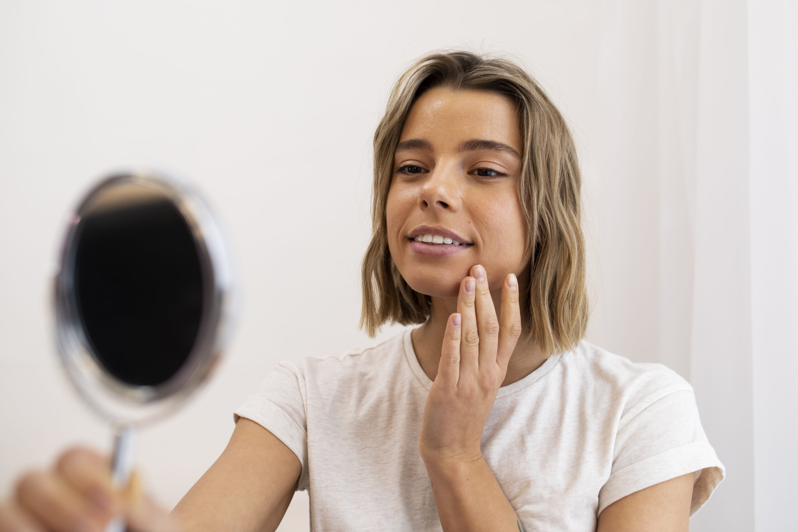 Woman smiles as she looks at her skin in a mirror