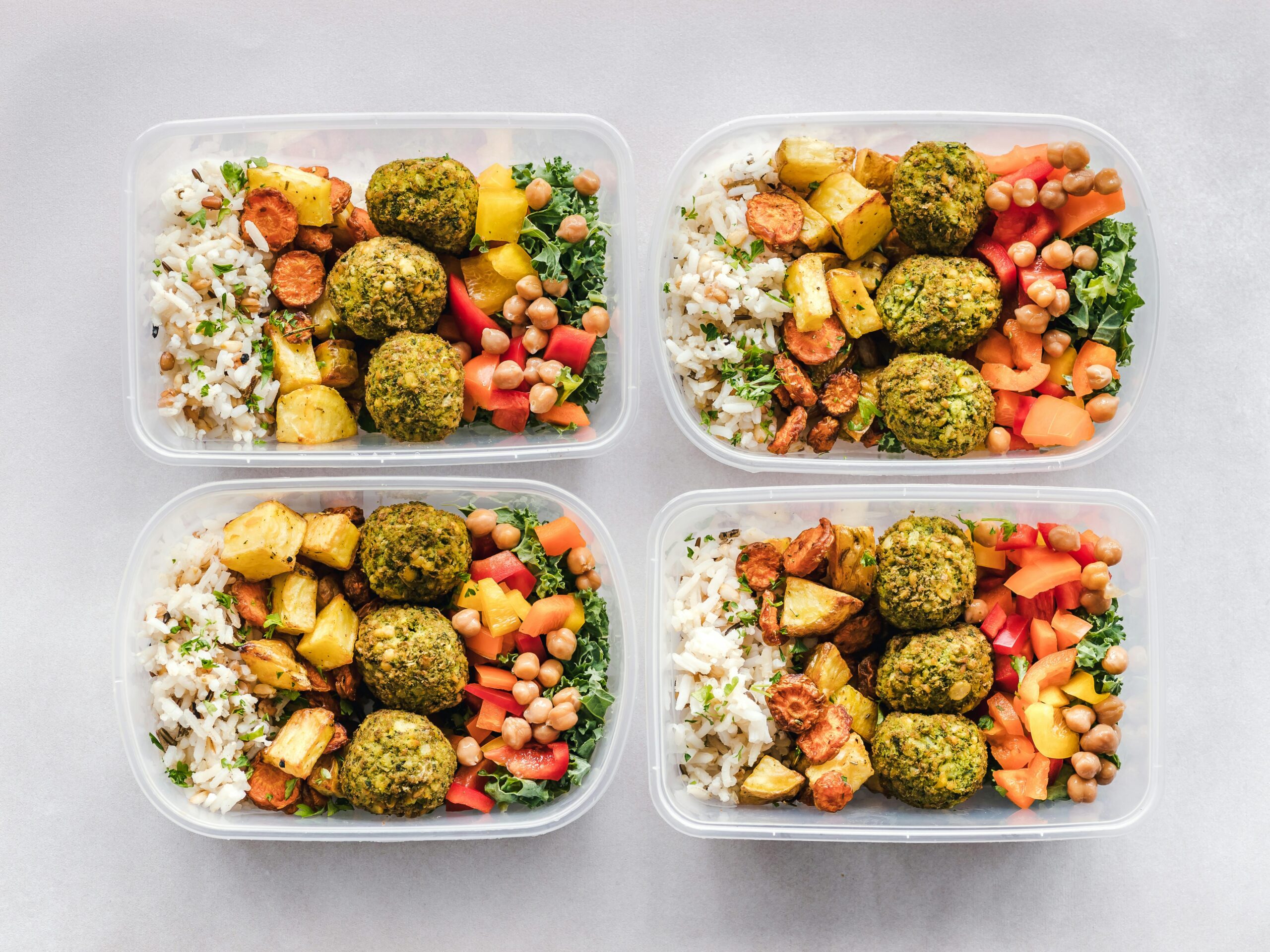 above view of four meal prep plastic pots with colourful balanced food in on grey white surface