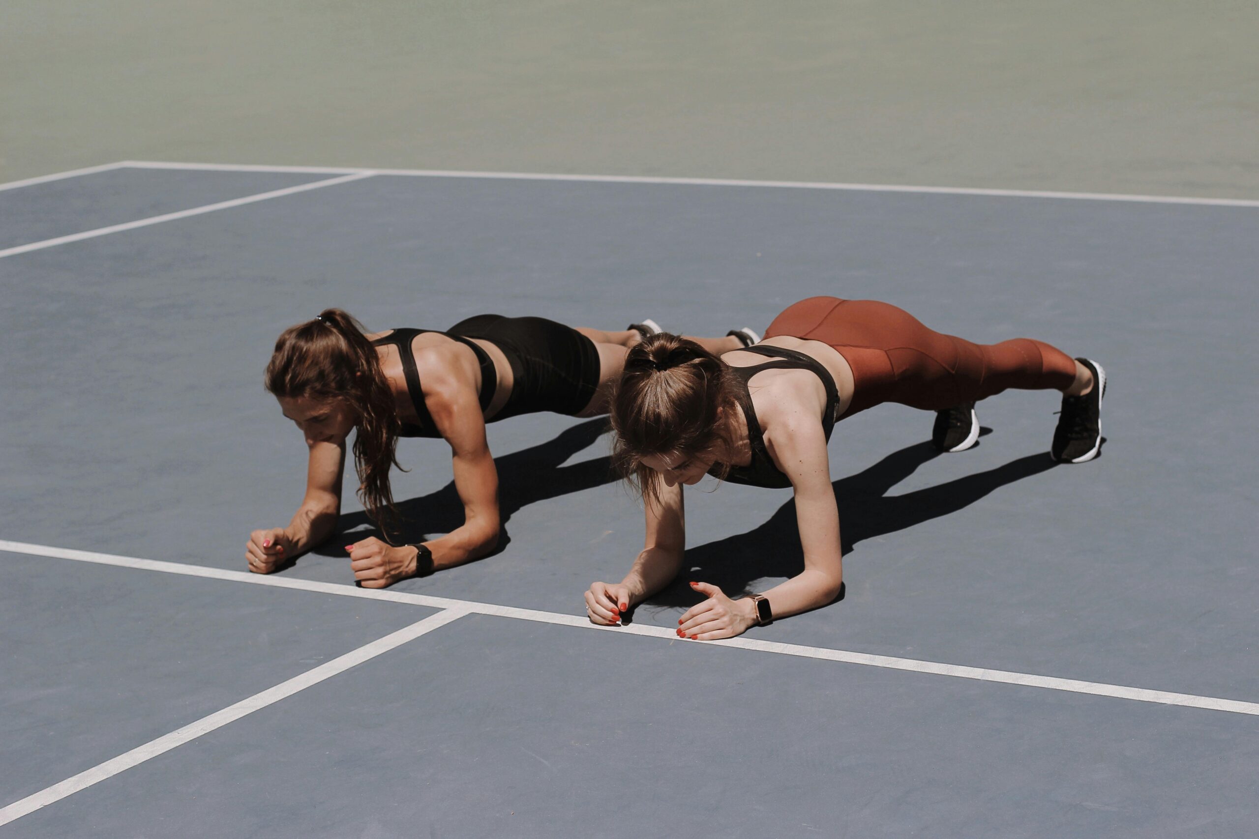 two women in a a blue tennis court planking in workout gear