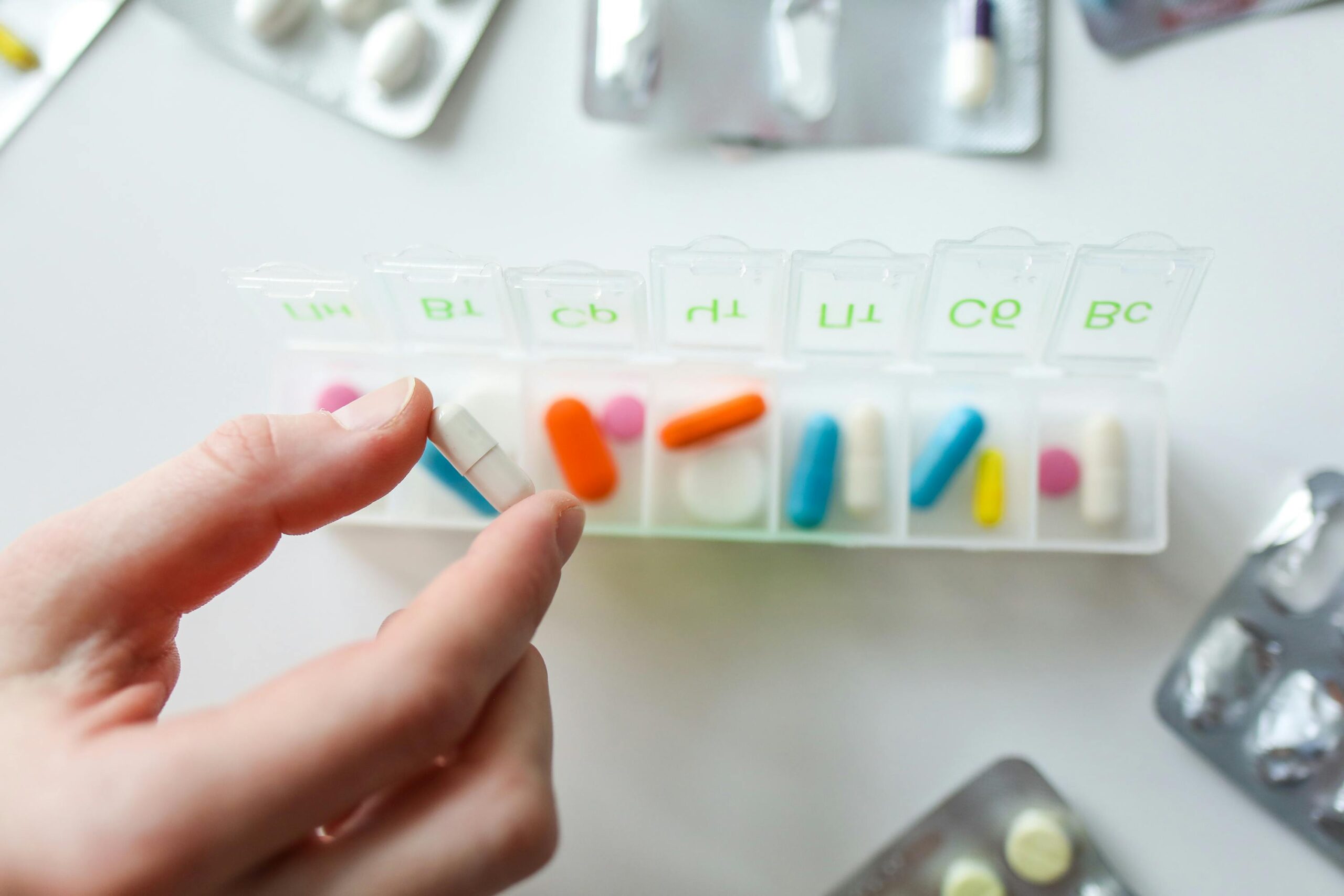 pill box with colourful meds and hand reaching in to take a white one