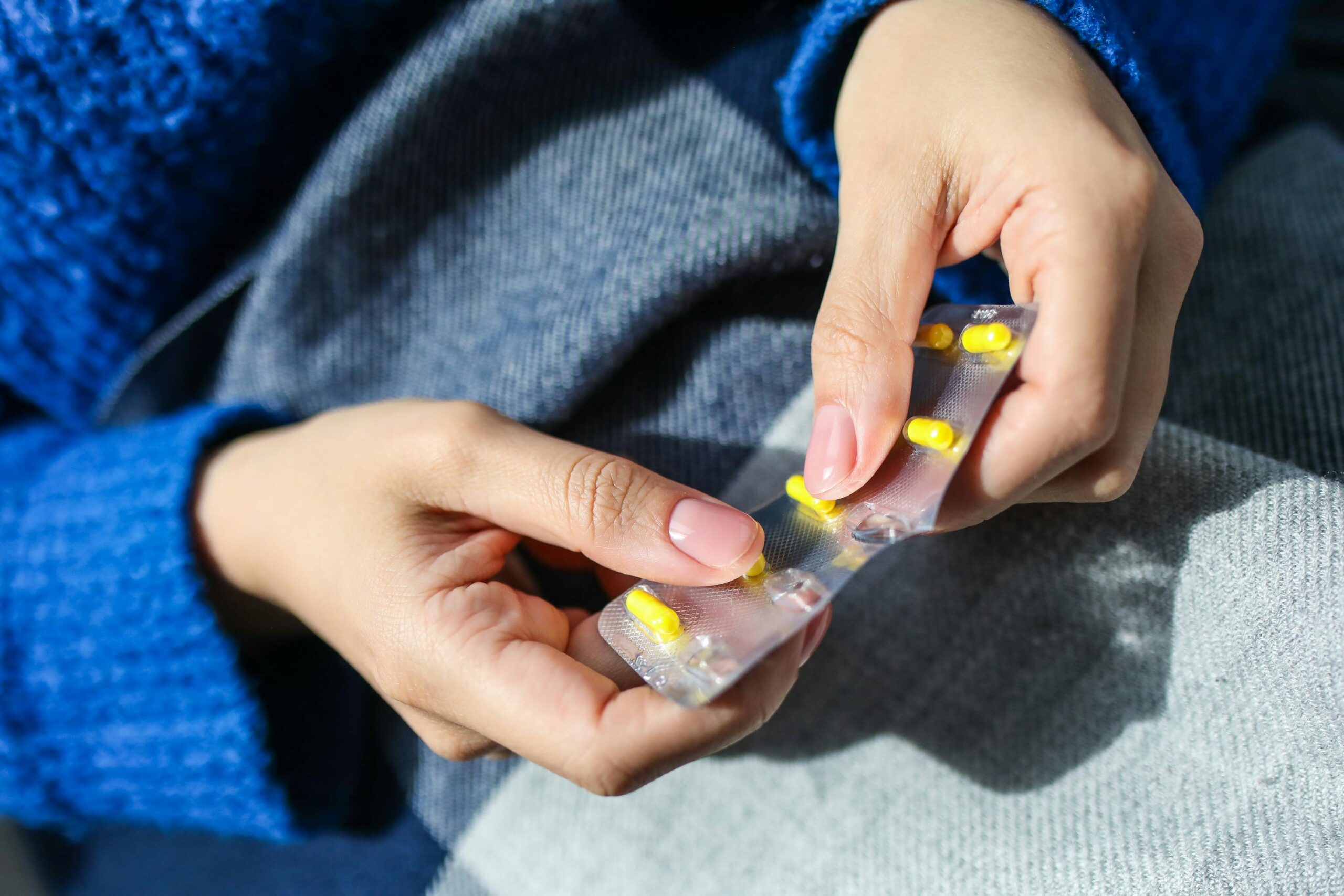 woman lap with jeans and blue jumper while her hands hold packet of yellow pill medication