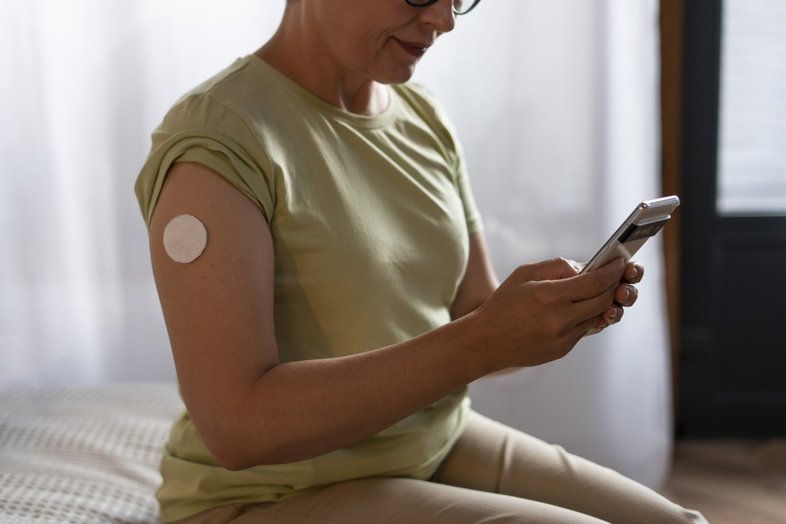 woman sitting down with green top with a circle medical patch on arm