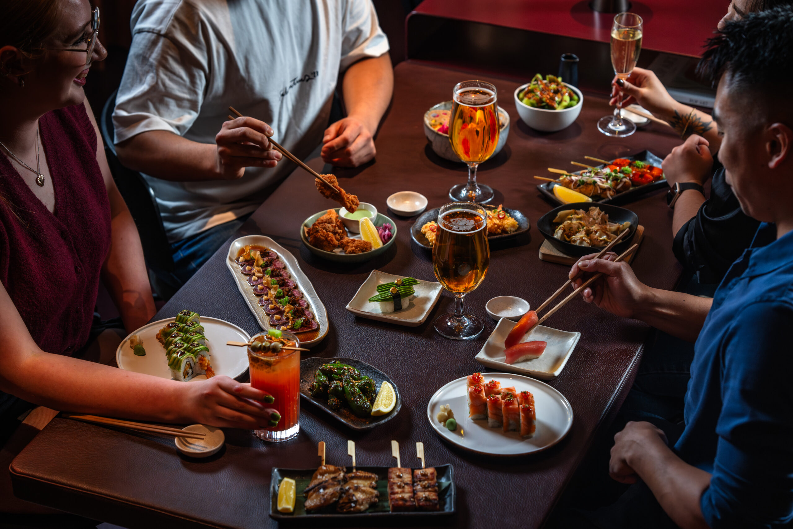 dark table with people sitting at the table eating sushi with chopsticks