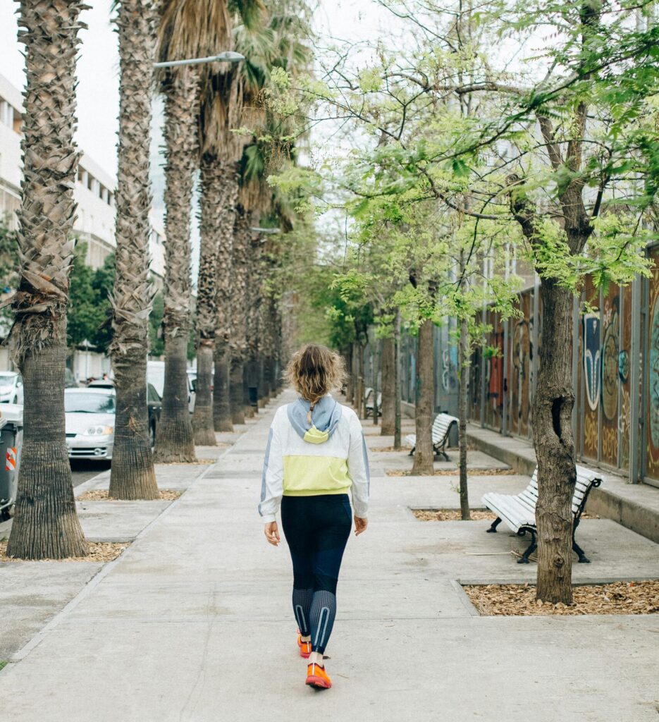 woman in workout clothes walking on pavement lined by trees