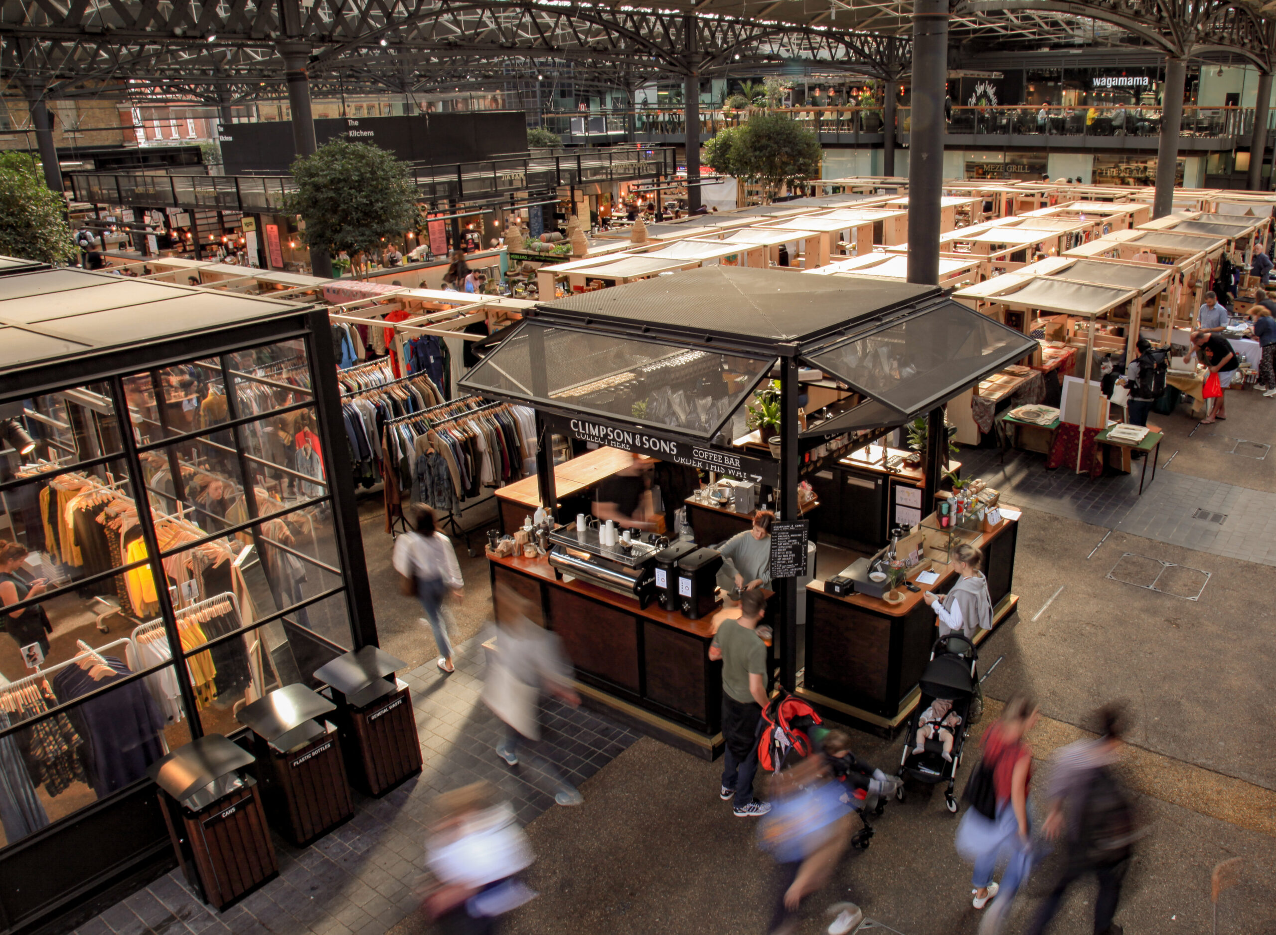 top side view of Spitalfields Market with stalls filled with clothes and a coffee shop with people bustling around