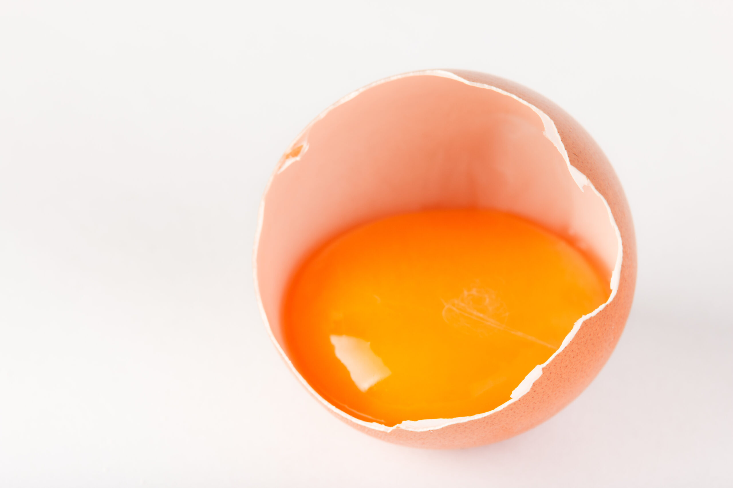 A raw egg yolk sat in an open egg shell.