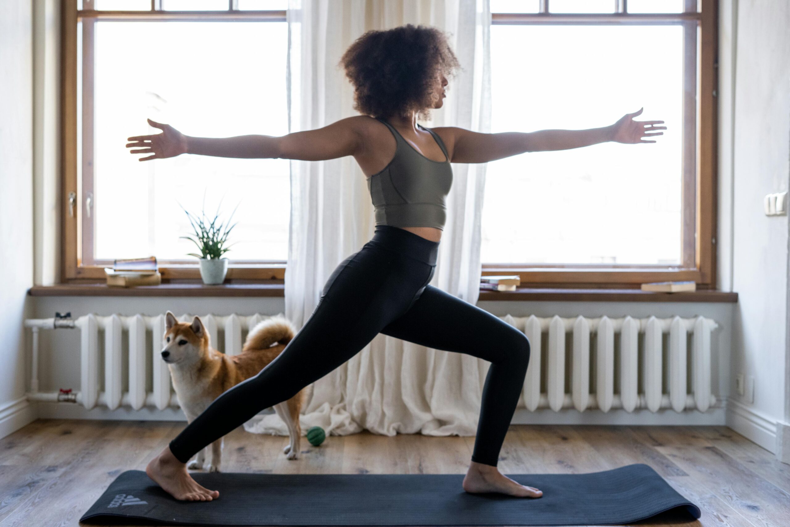 woman in home on yoga mat in black leggings and slate grey top doing moderate yoga intensity pose
