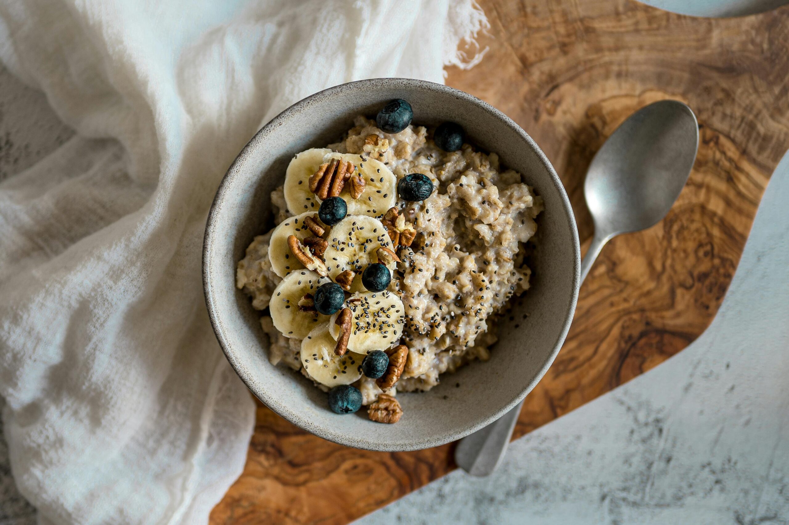 Wooden table with marble bit spoon bowl with oatmeal, bananas berries and chia seeds on top