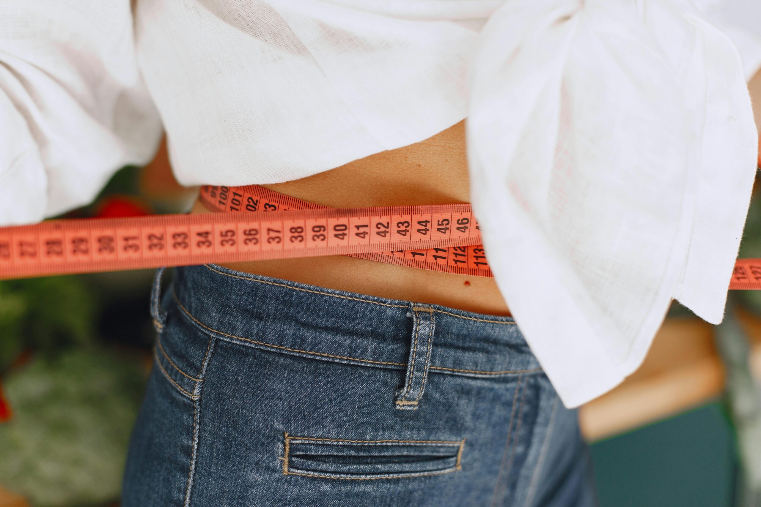 woman's torso in jeans and white shirt holding a measuring tape around the waist