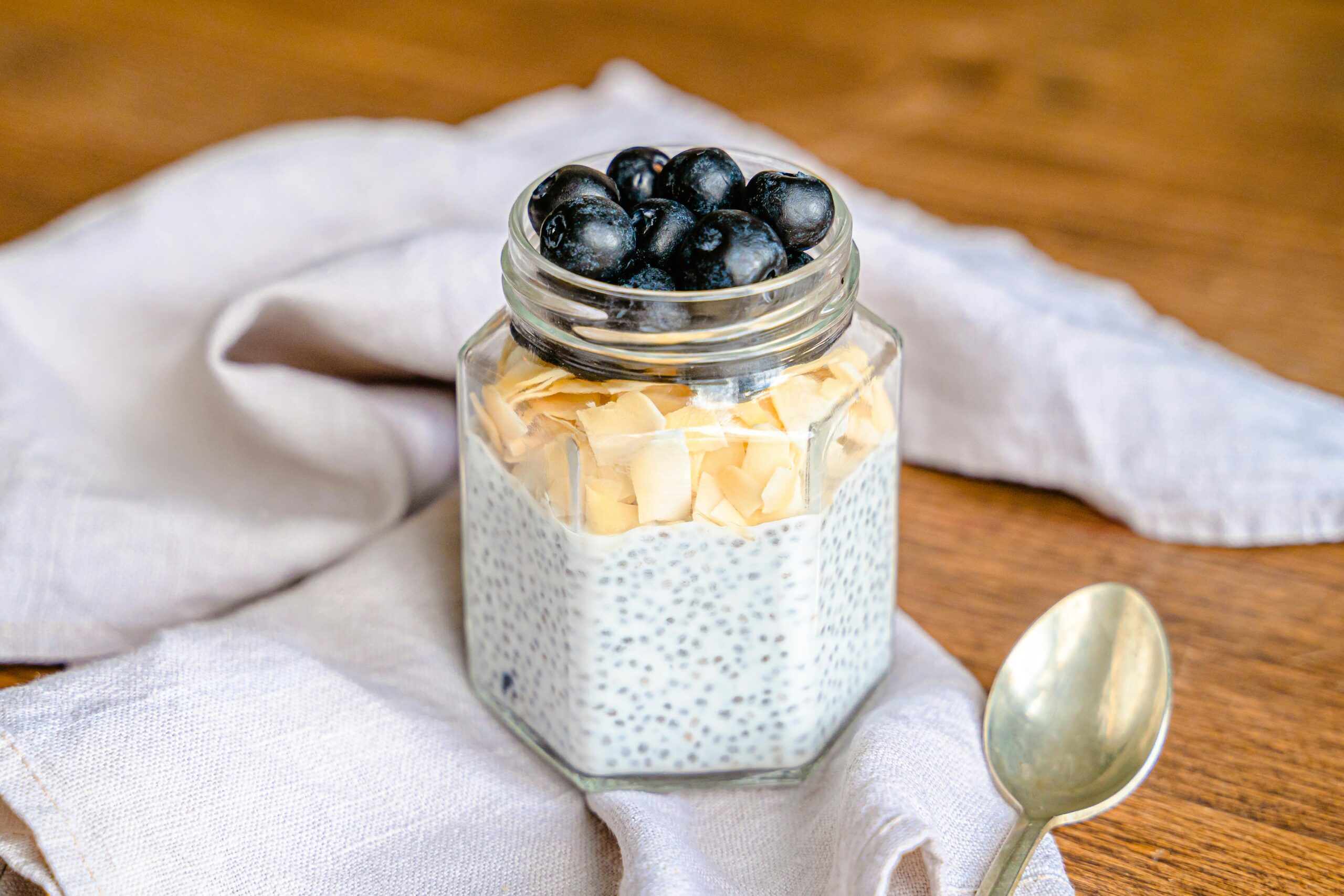 wooden table with grey kitchen cloth and jar with yoghurt and chia seeds and berries