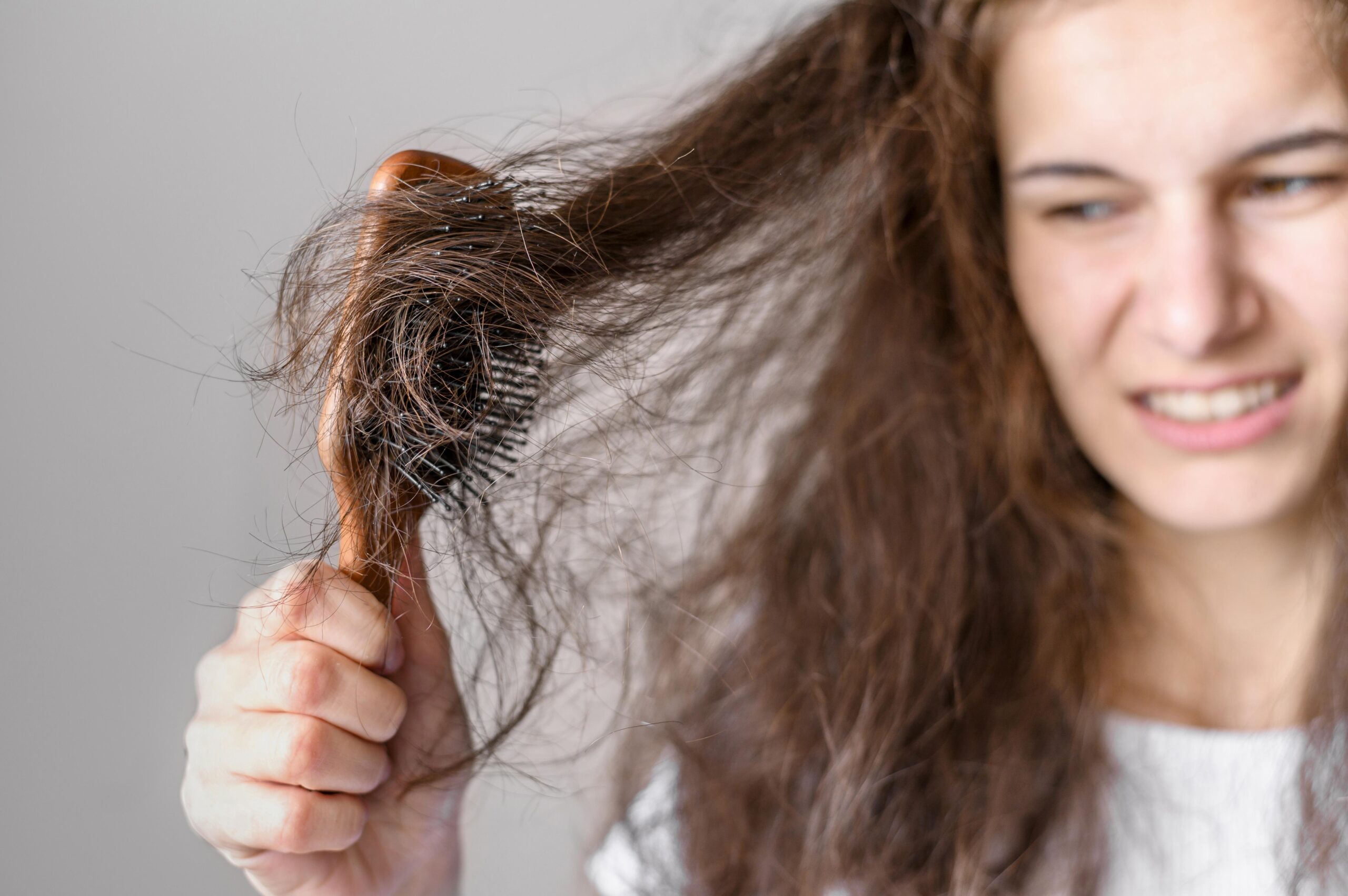 woman with brown hair struggling to pull brown wooden hair brush through her hair and looking frustrated