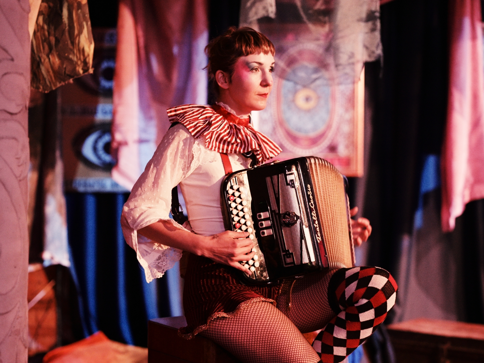 woman in circus gear sitting on a stool playing the accordion at a halloween event